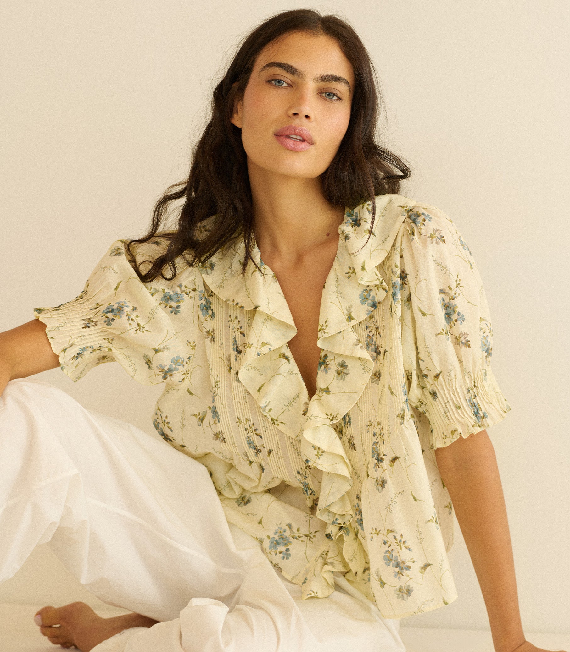 Woman wearing a light yellow floral blouse with ruffled sleeves on a plain background 1
