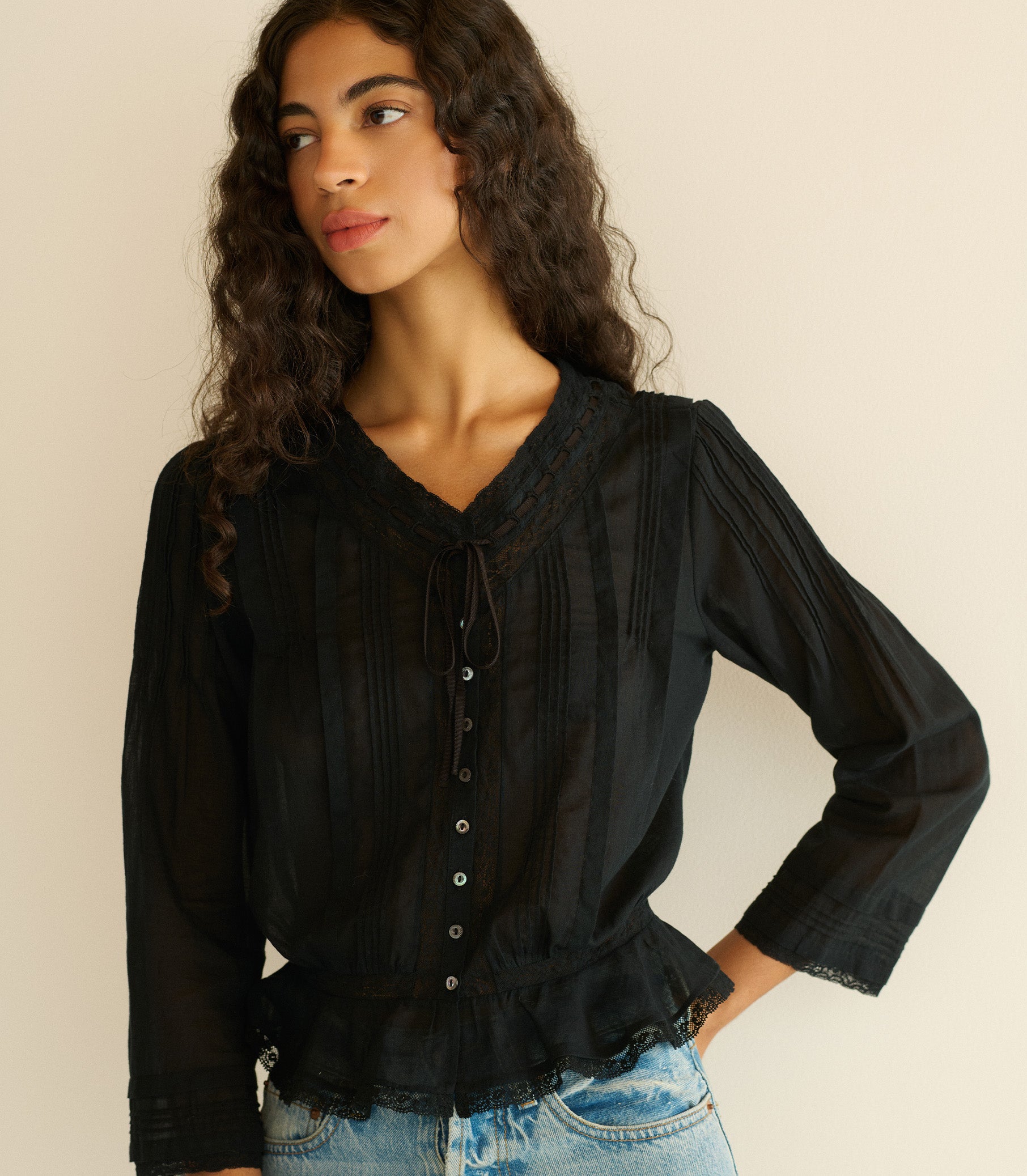 Woman wearing a black blouse with long sleeves against a beige background 1
