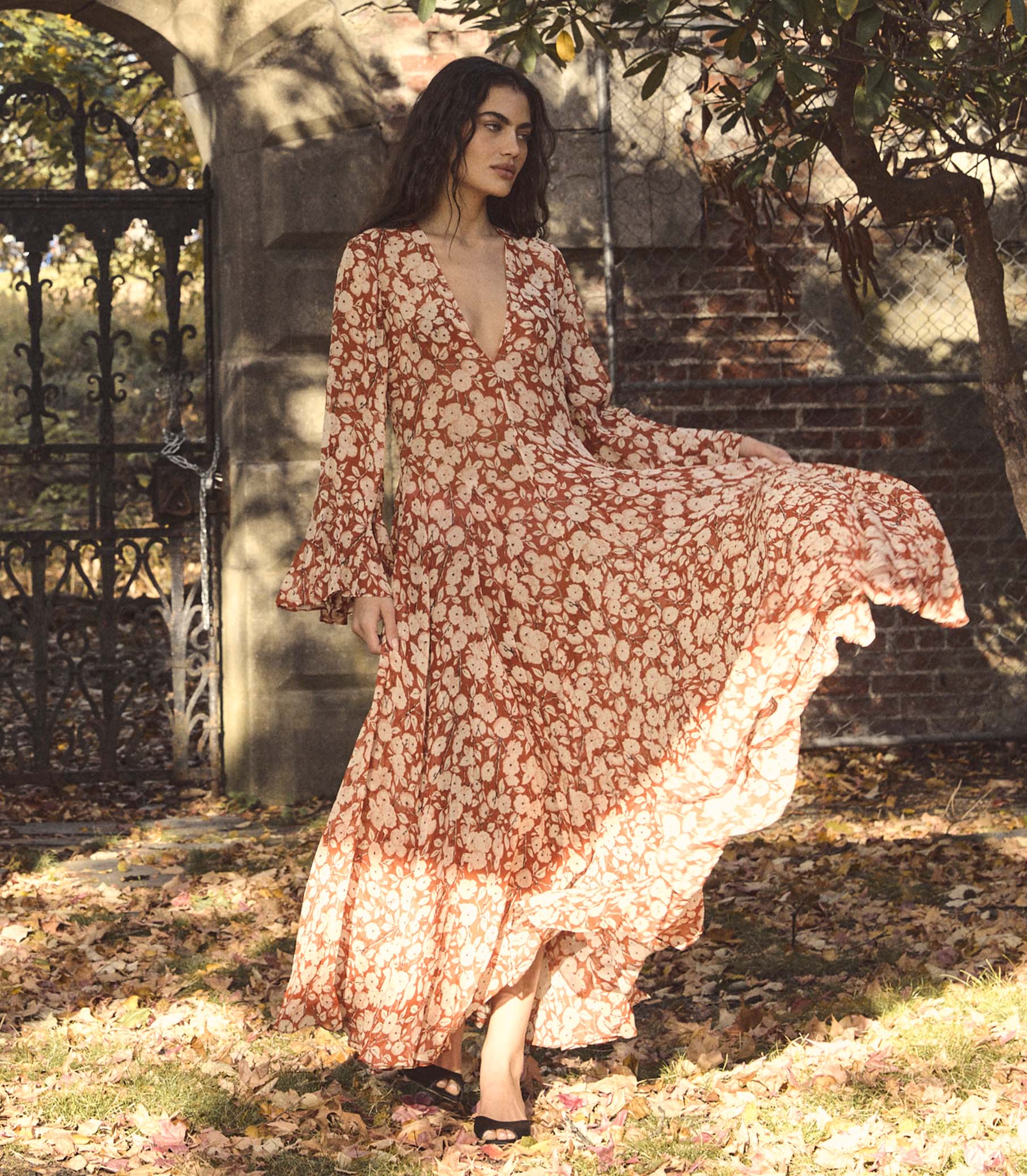 Woman in a red floral dress standing outdoors with trees and a gate in the background 1
