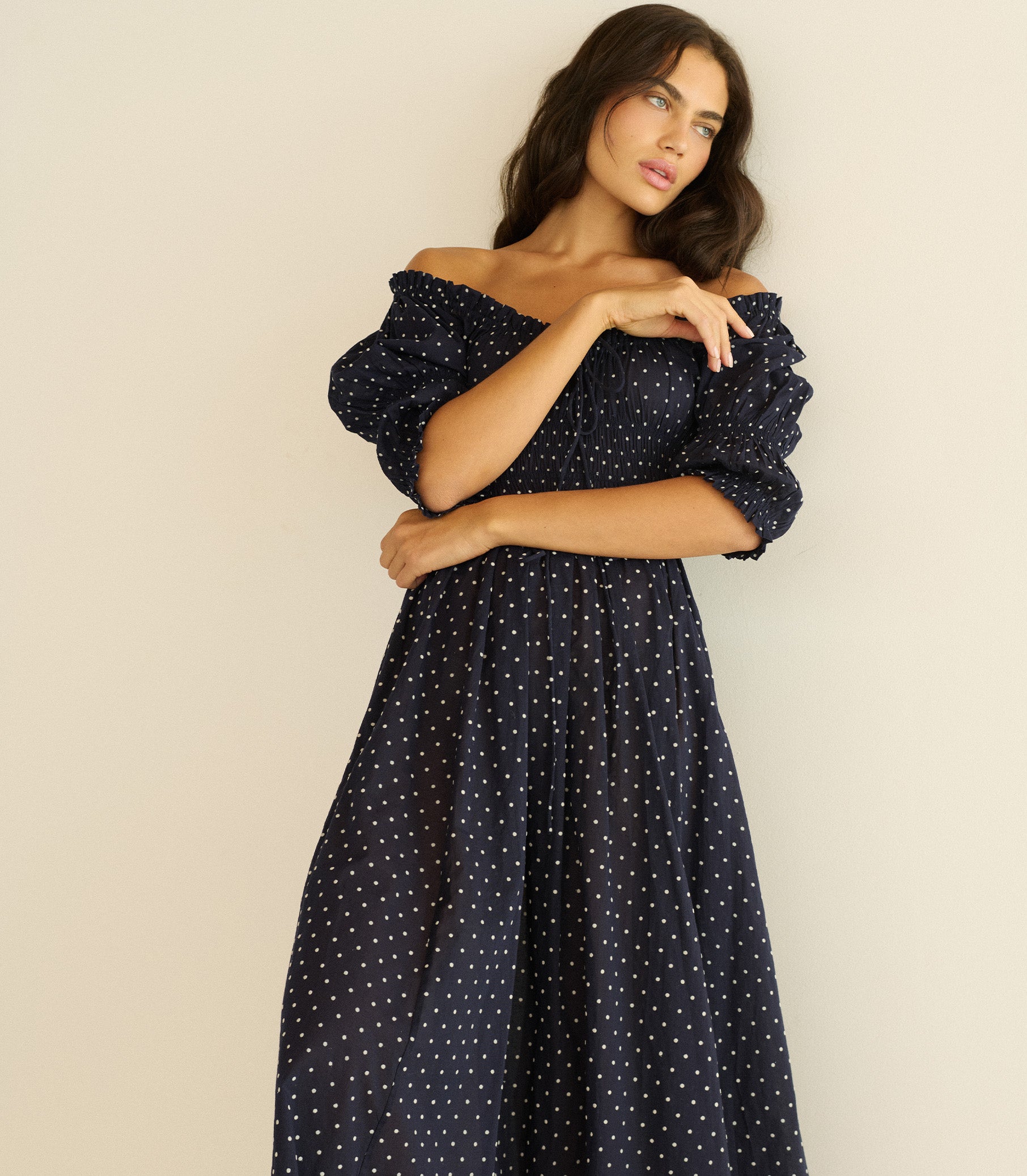Woman wearing a navy blue dress with white polka dots against a beige background 1
