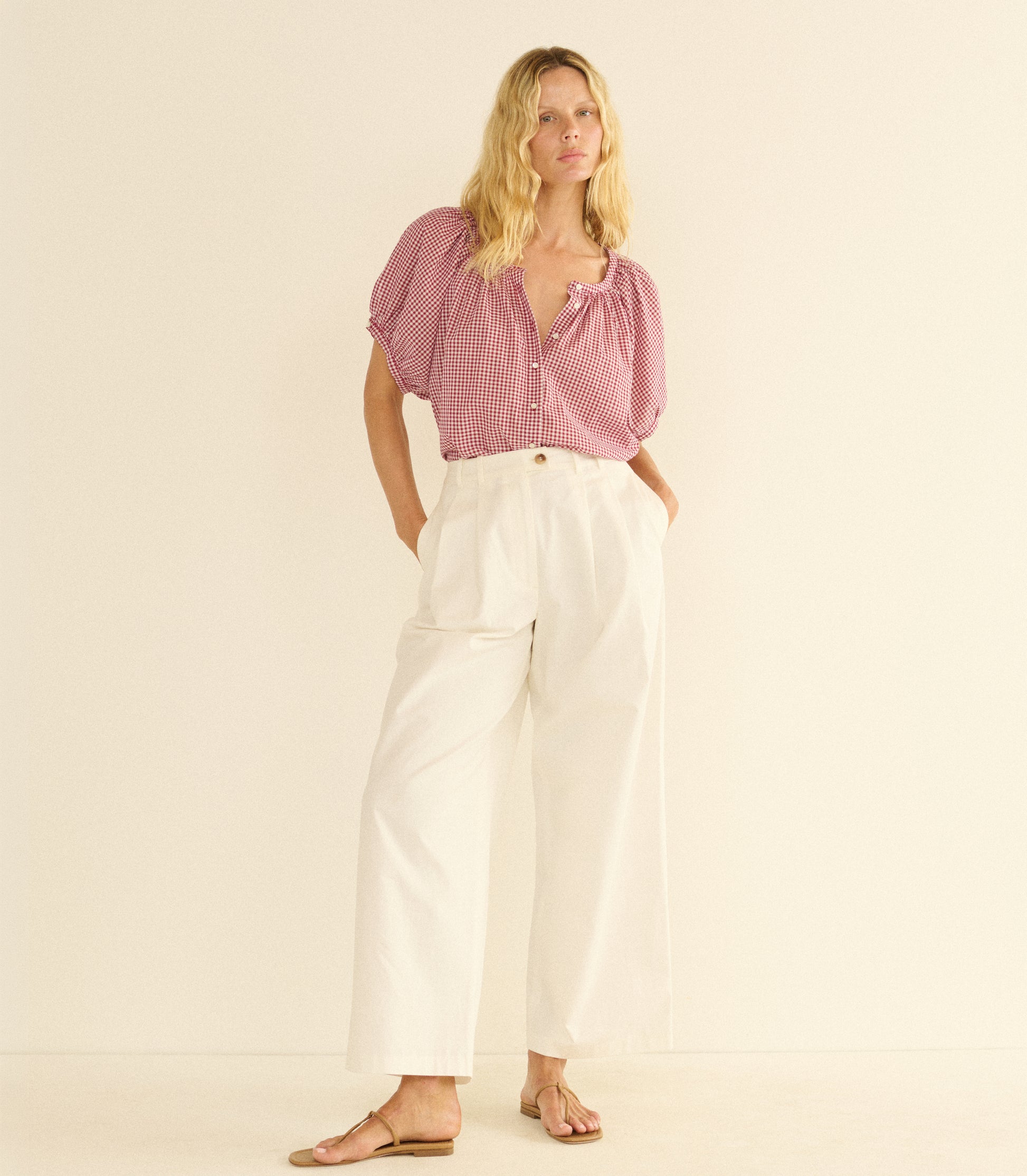 Woman wearing a red checkered blouse and white pants on a beige background 1

