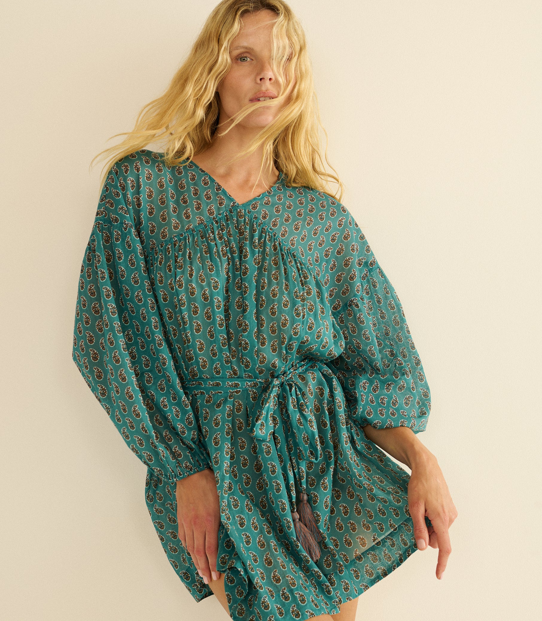 Woman wearing a teal patterned dress against a beige background