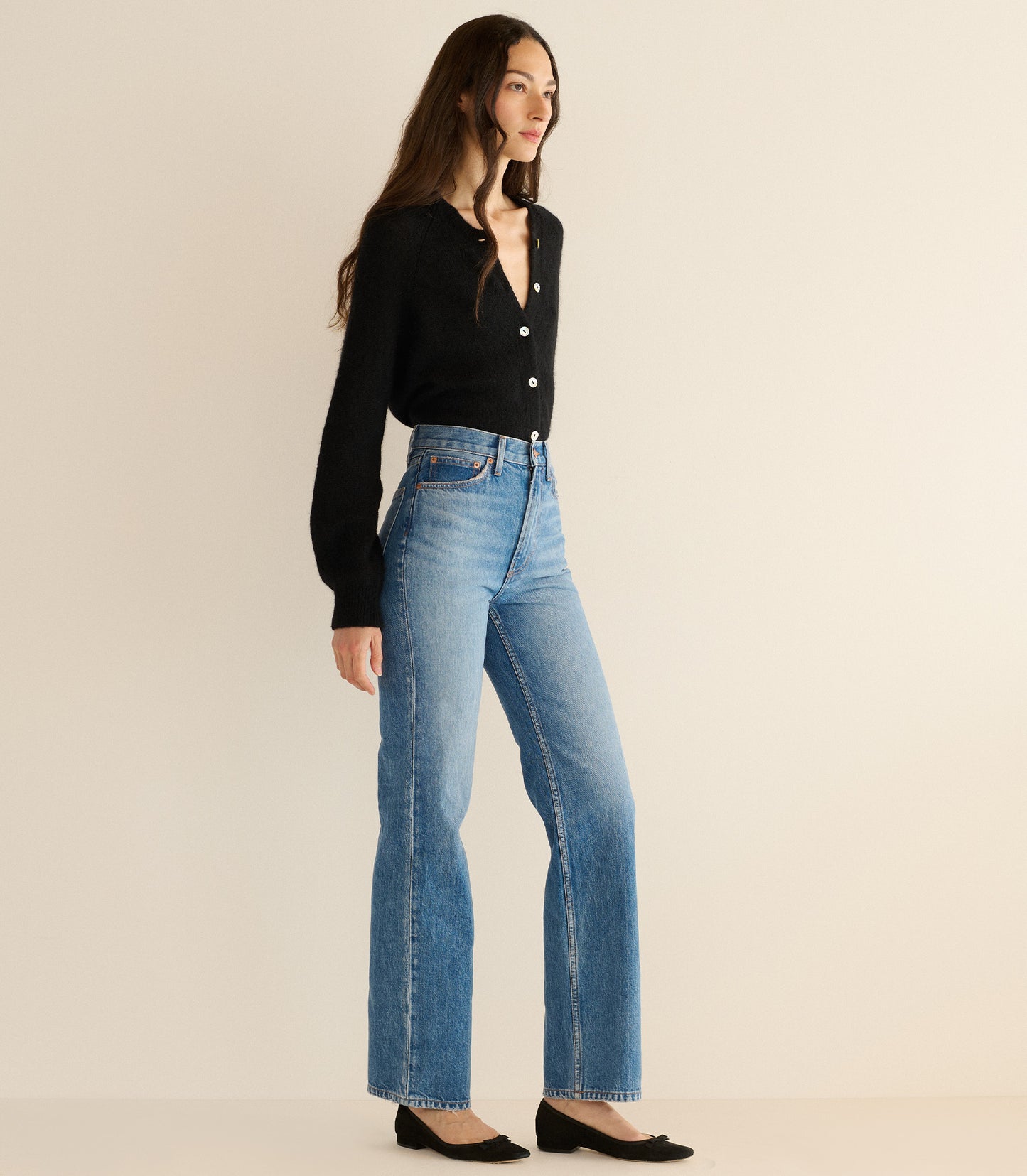 Woman wearing a black cardigan and blue jeans on a beige background