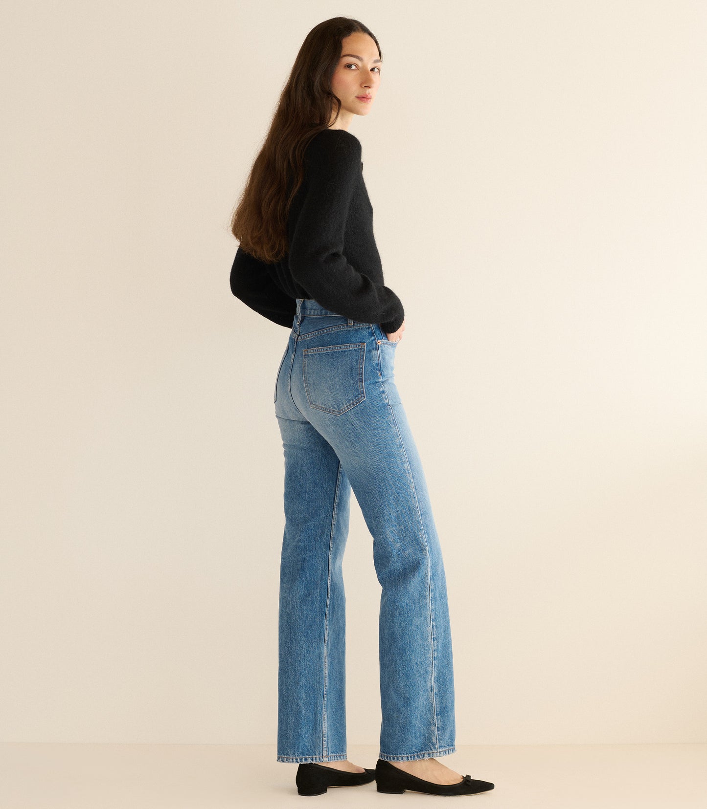 Woman wearing a black cardigan and blue jeans on a beige background