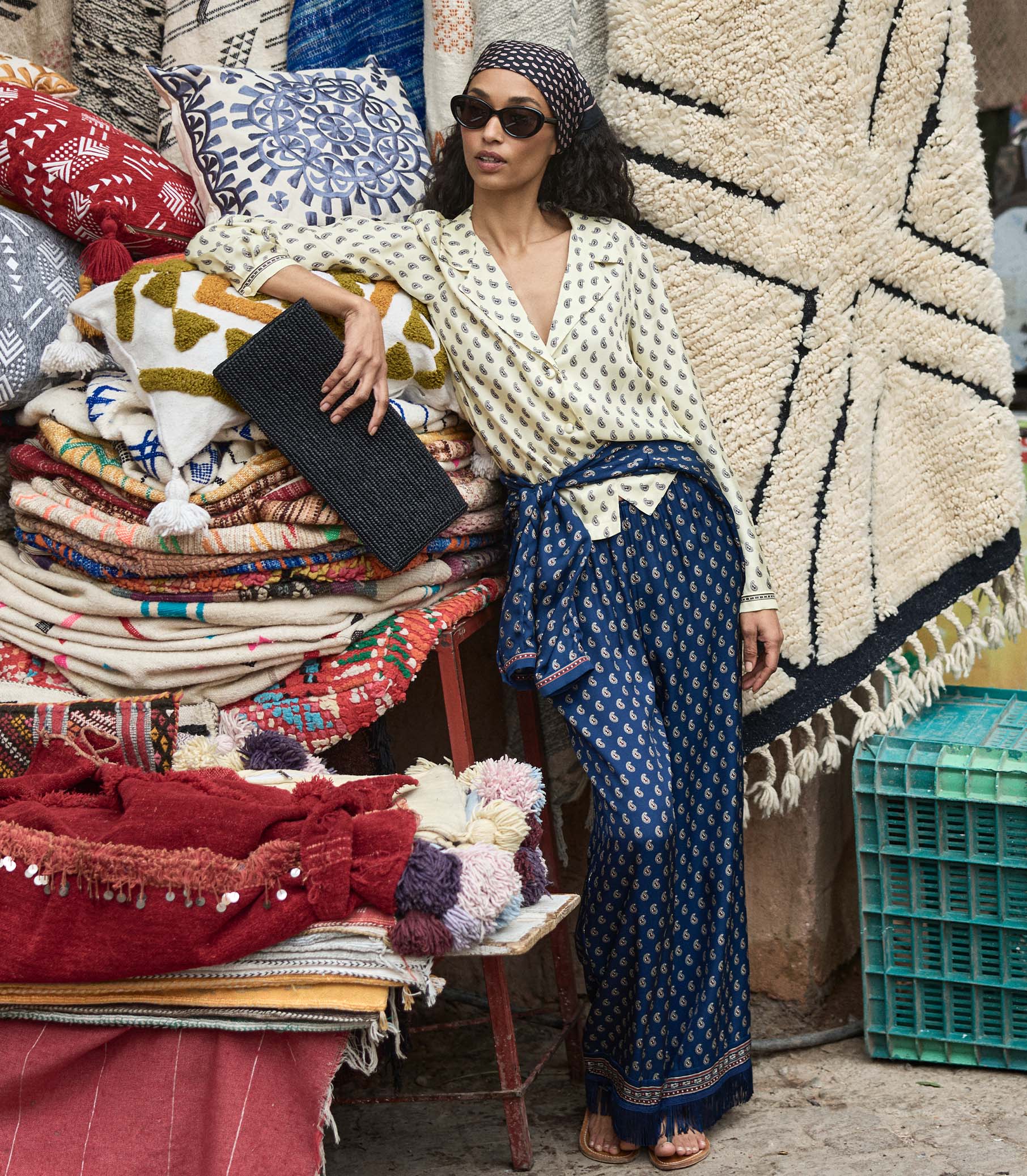 Woman in a paisley blouse and pants in a  market setting surrounded by colorful fabrics and rugs 1
