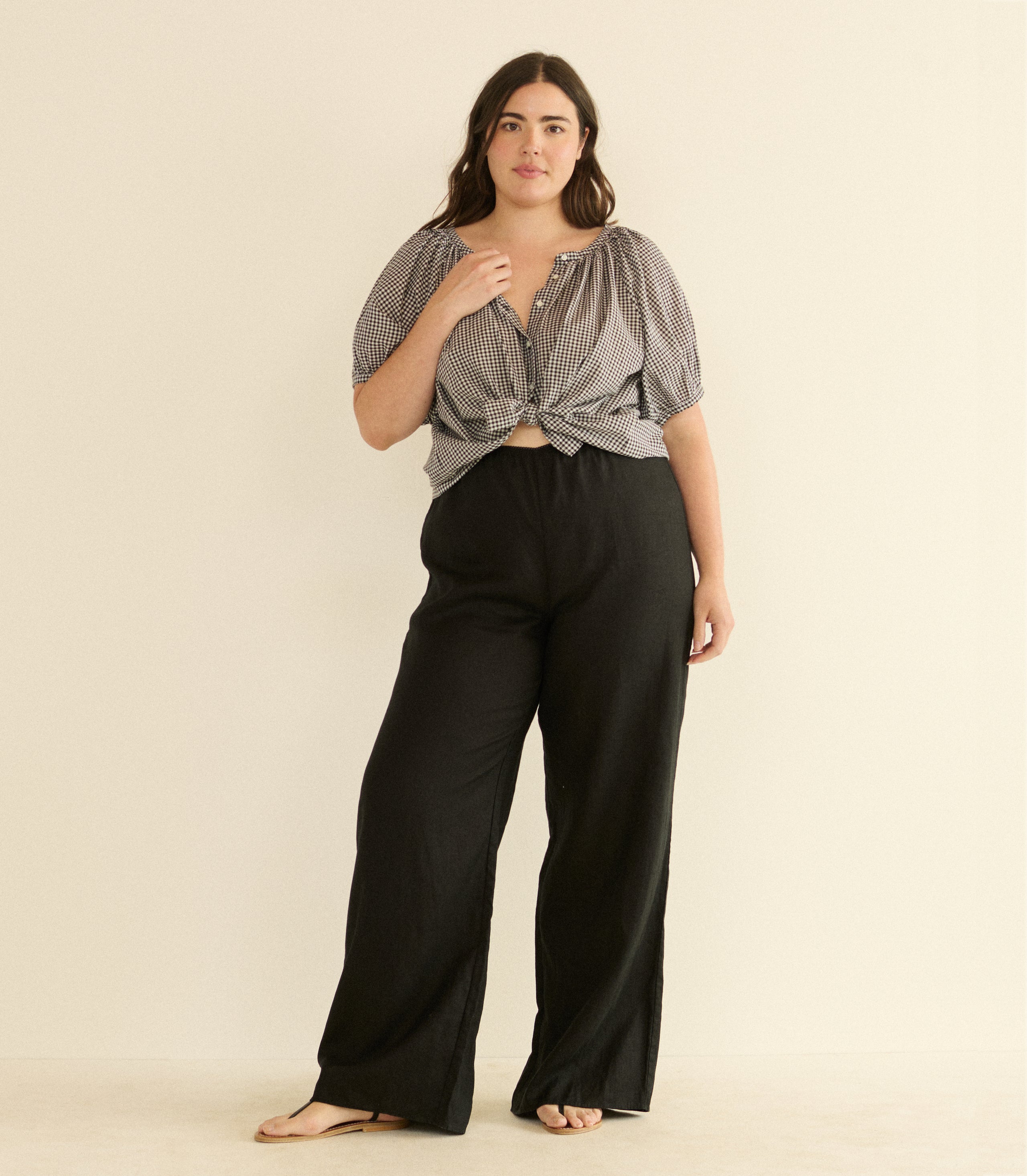 Woman wearing a black and white checkered top and black pants on a beige background