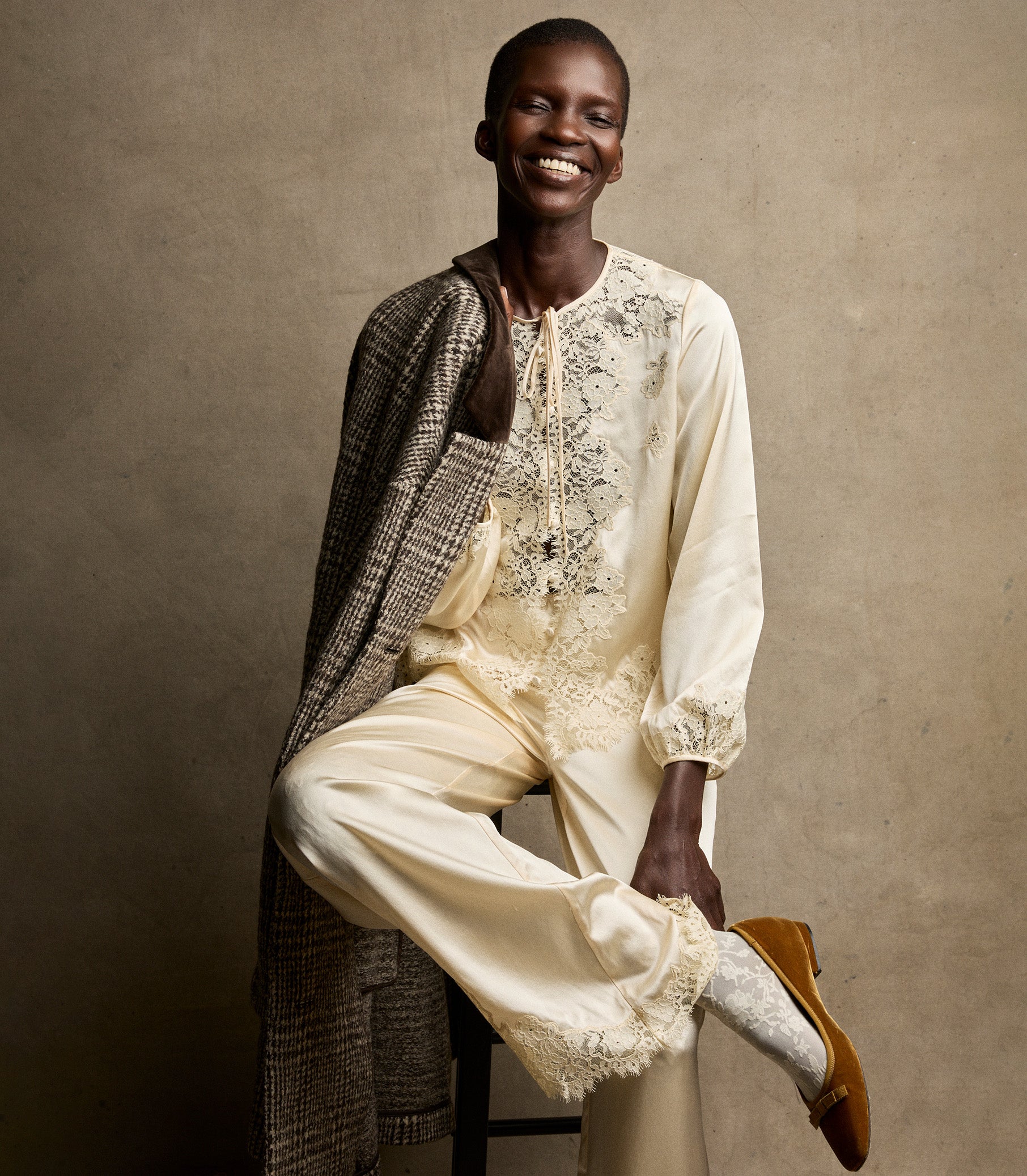 Person wearing a cream-colored outfit with intricate lace against a beige background 8
