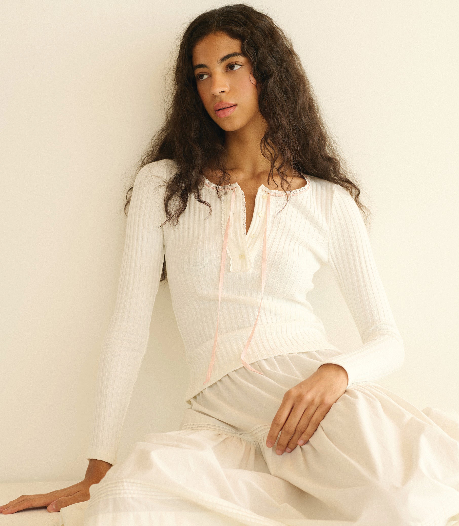 Woman wearing a white knit tee sitting against a plain background 1
