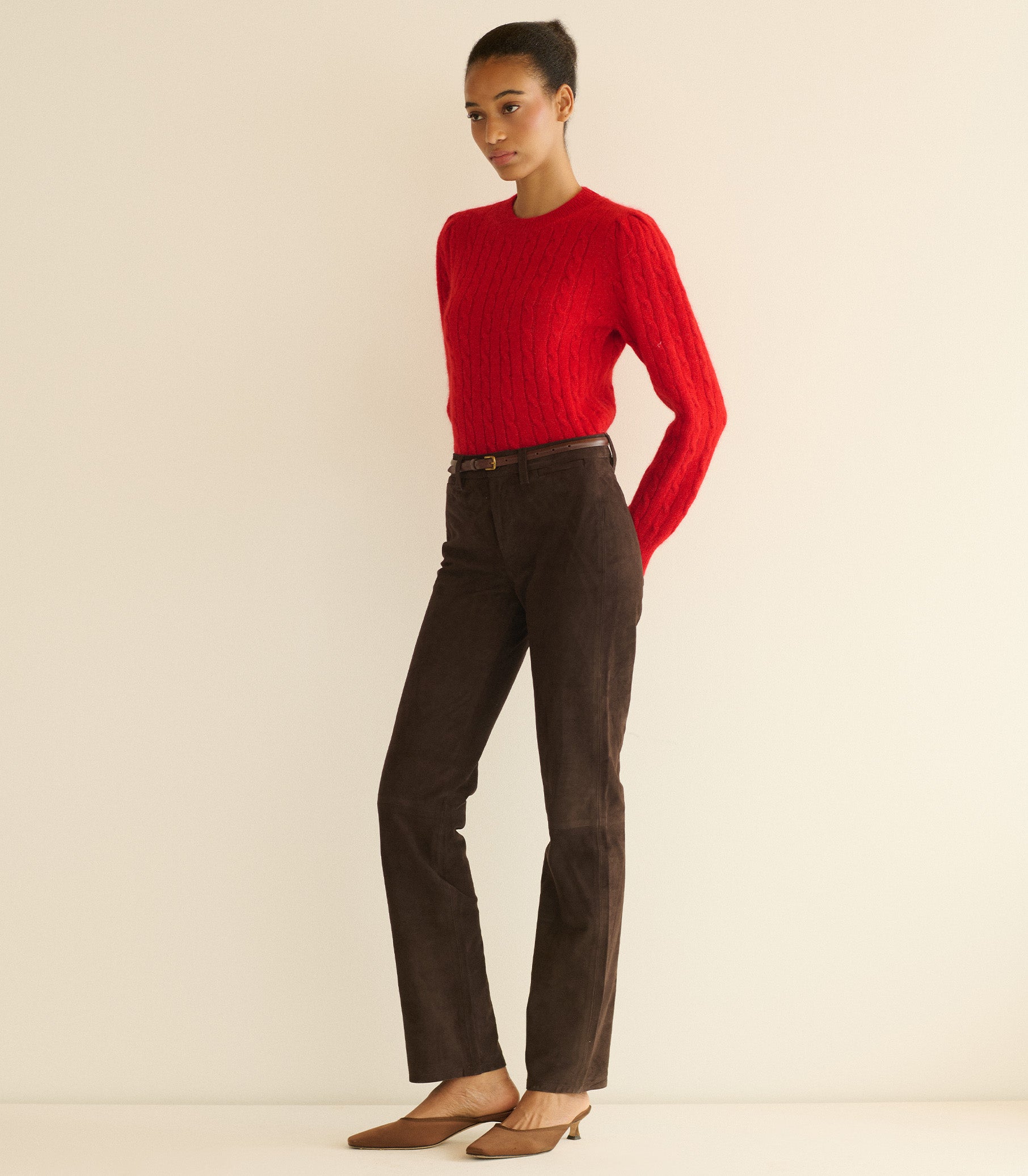 Person wearing a red sweater and brown pants on a beige background 2
