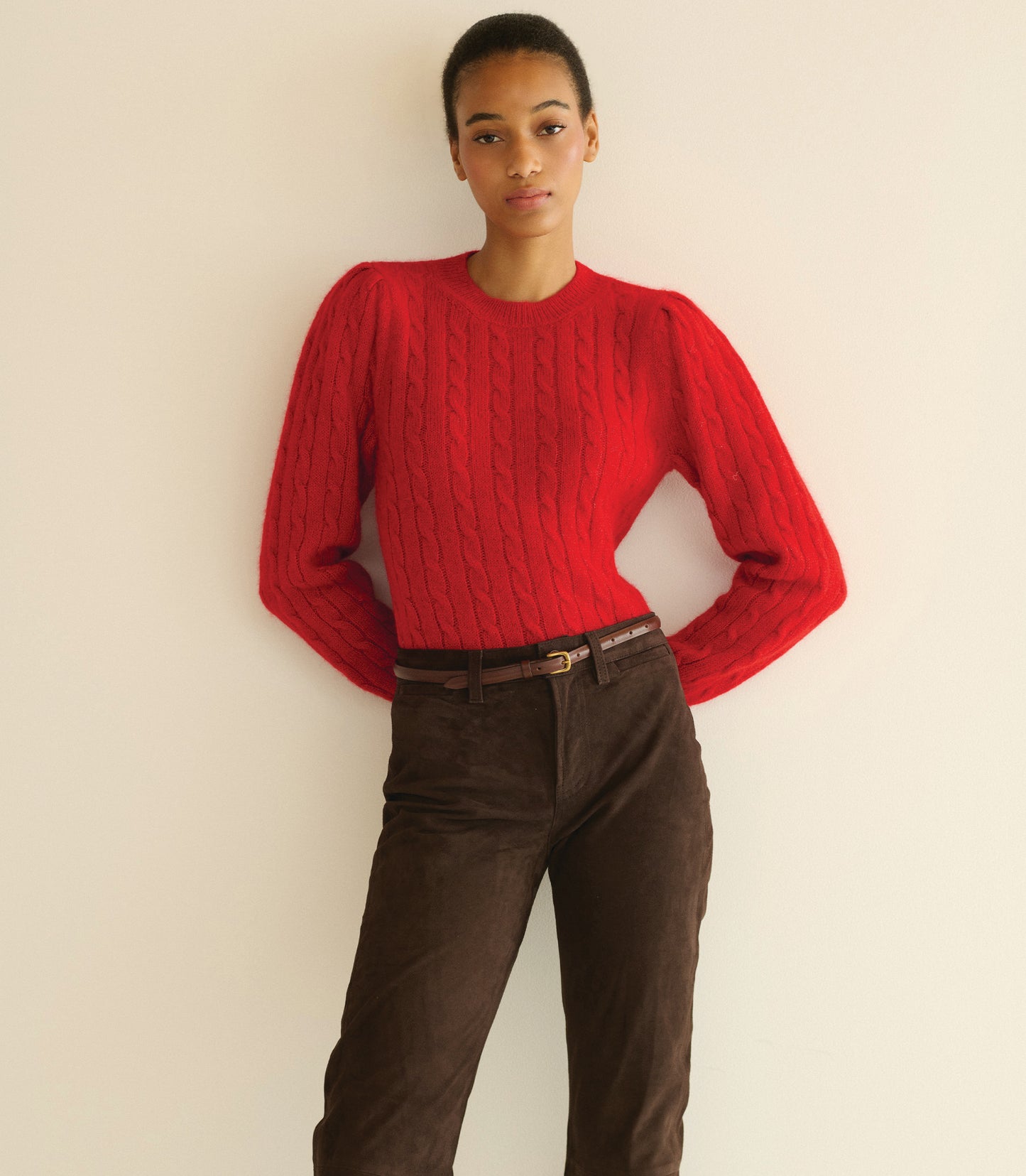 Person wearing a red sweater and brown pants against a plain background