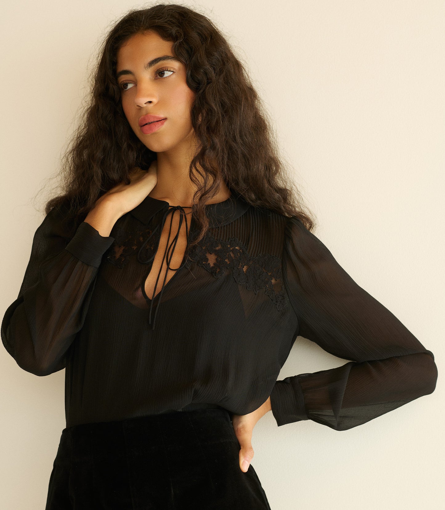 Woman wearing a black blouse with sheer sleeves against a plain background