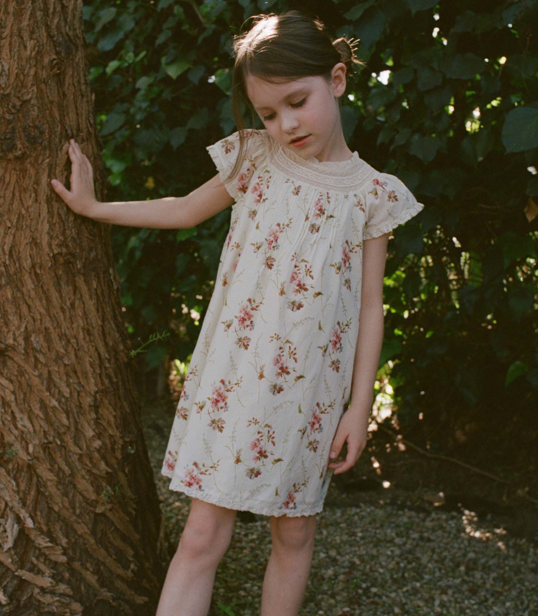 Young girl in a floral dress standing next to a tree in a natural setting 1
