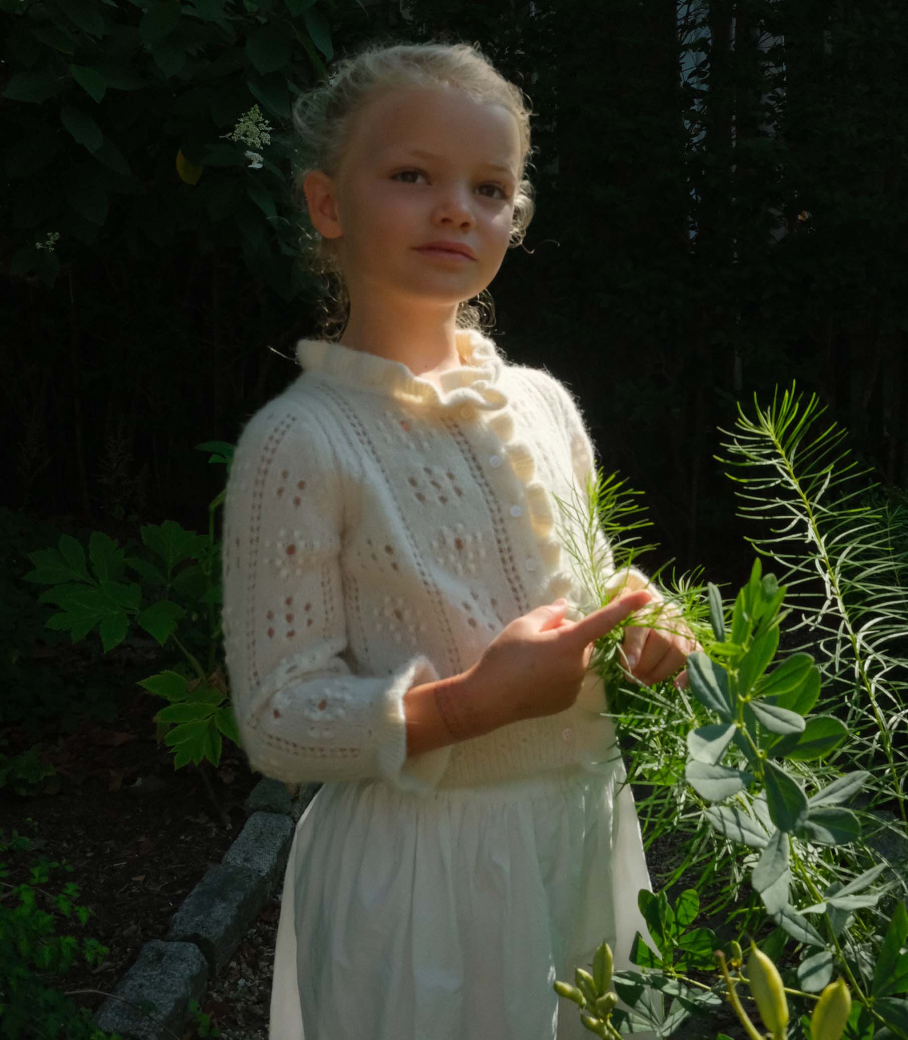 Young girl in a white dress standing among plants 1
