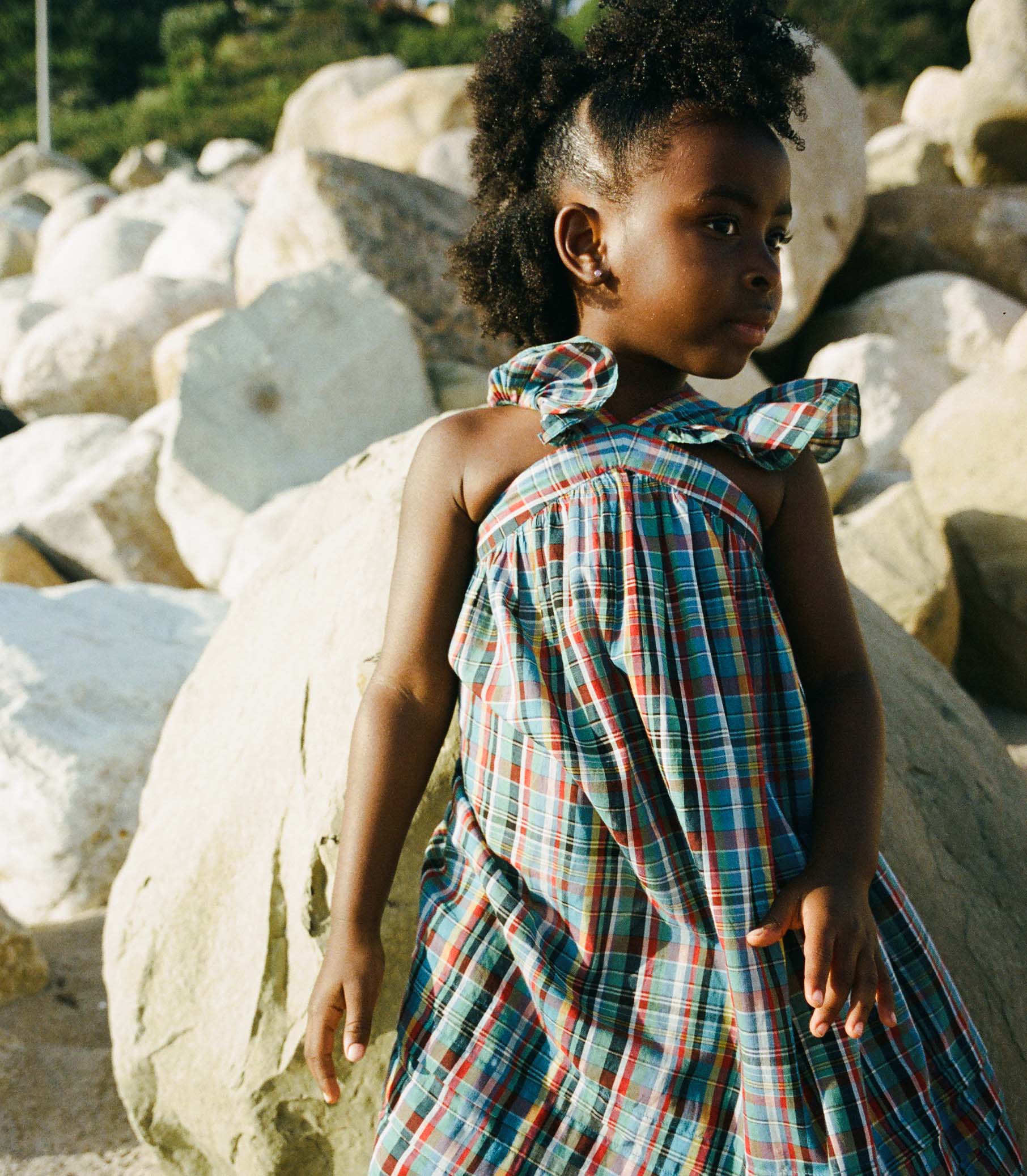 Young girl in a plaid dress standing among large rocks.