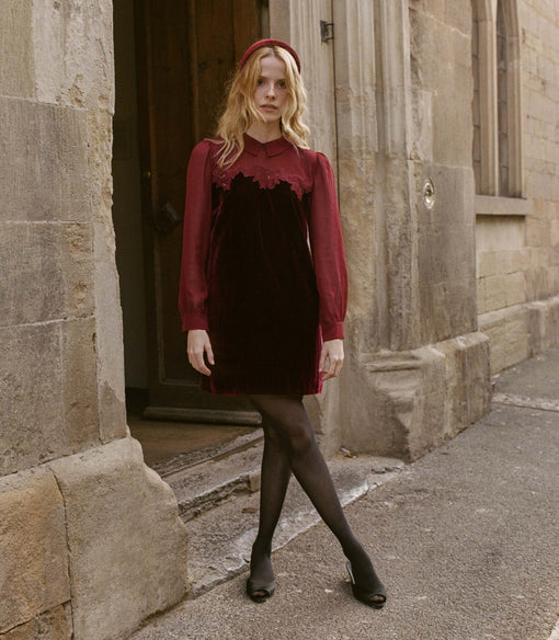 Woman in a red velvet dress standing in front of a stone building.