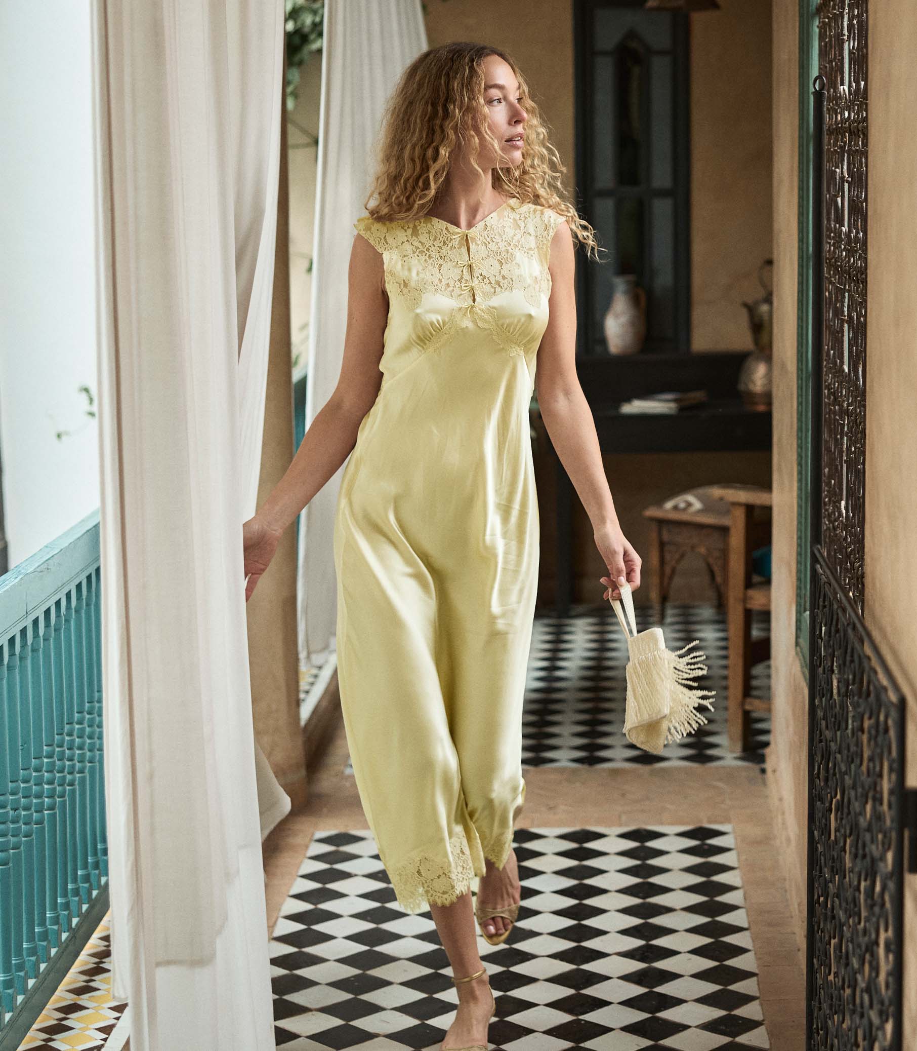 Woman in a yellow silk dress walking through a doorway with a checkered floor.