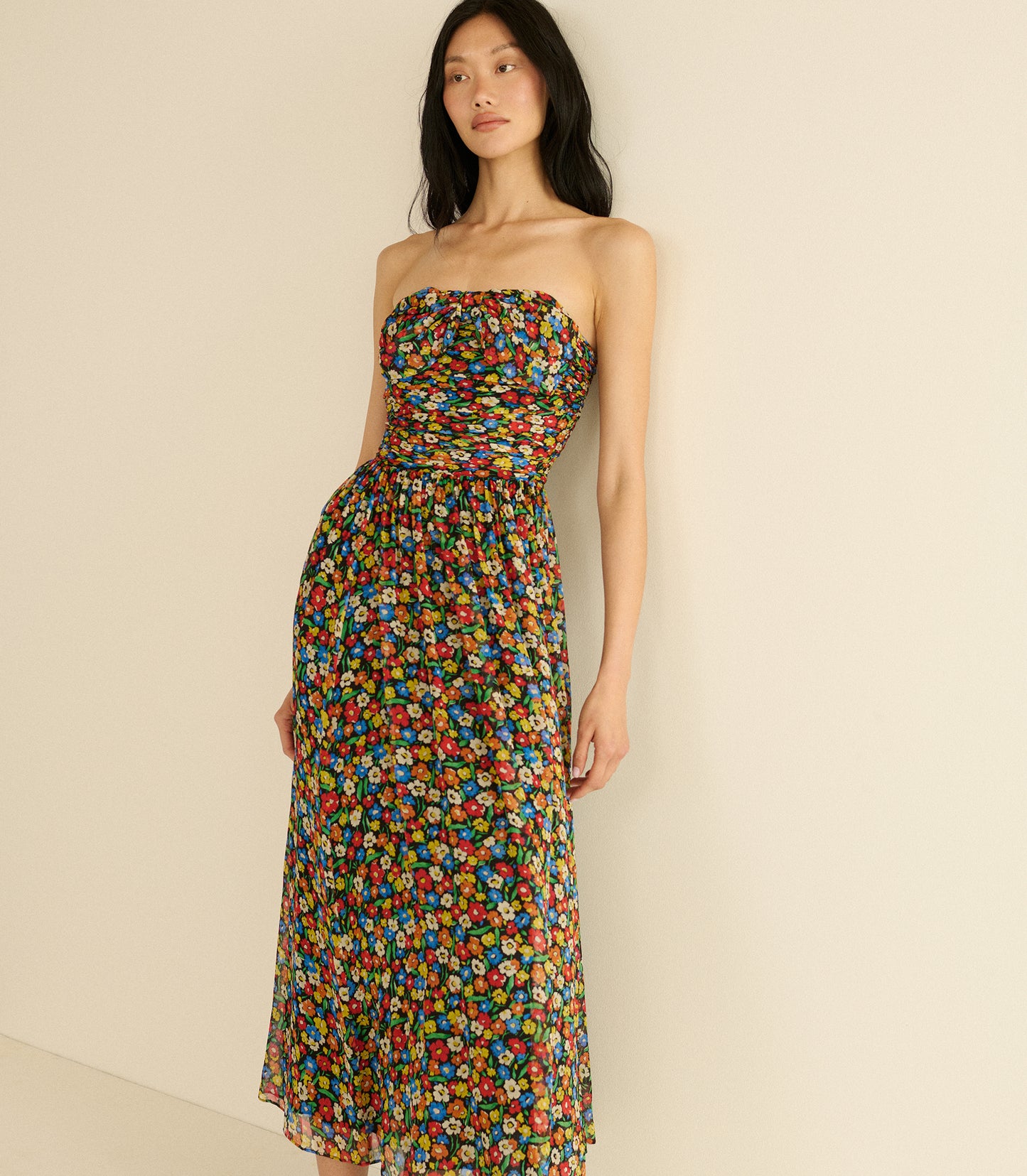 Woman wearing a strapless, multicolored floral dress against a beige background