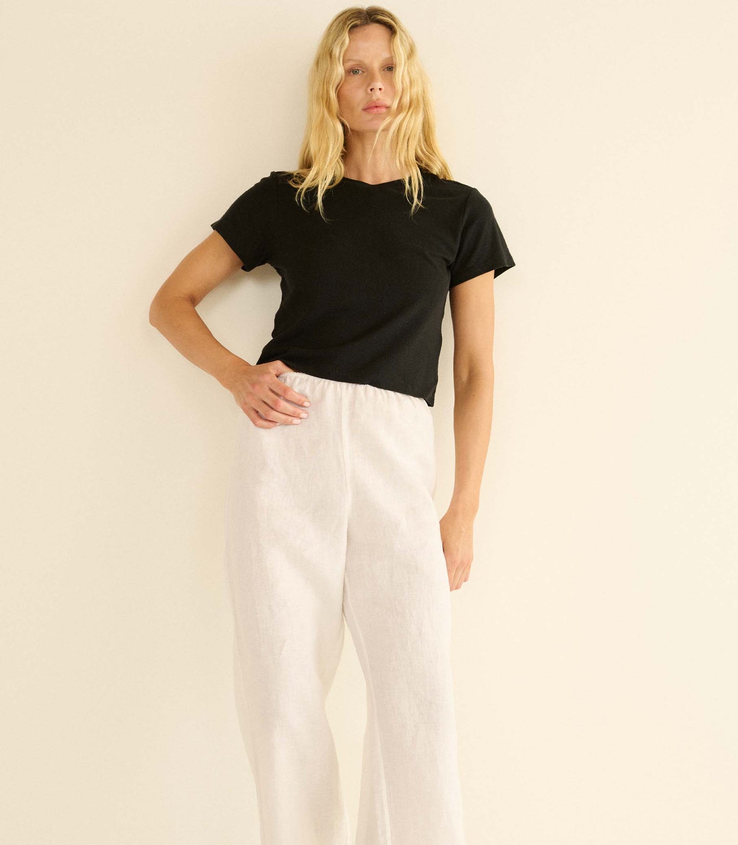 Woman wearing a black t-shirt and white pants against a beige background