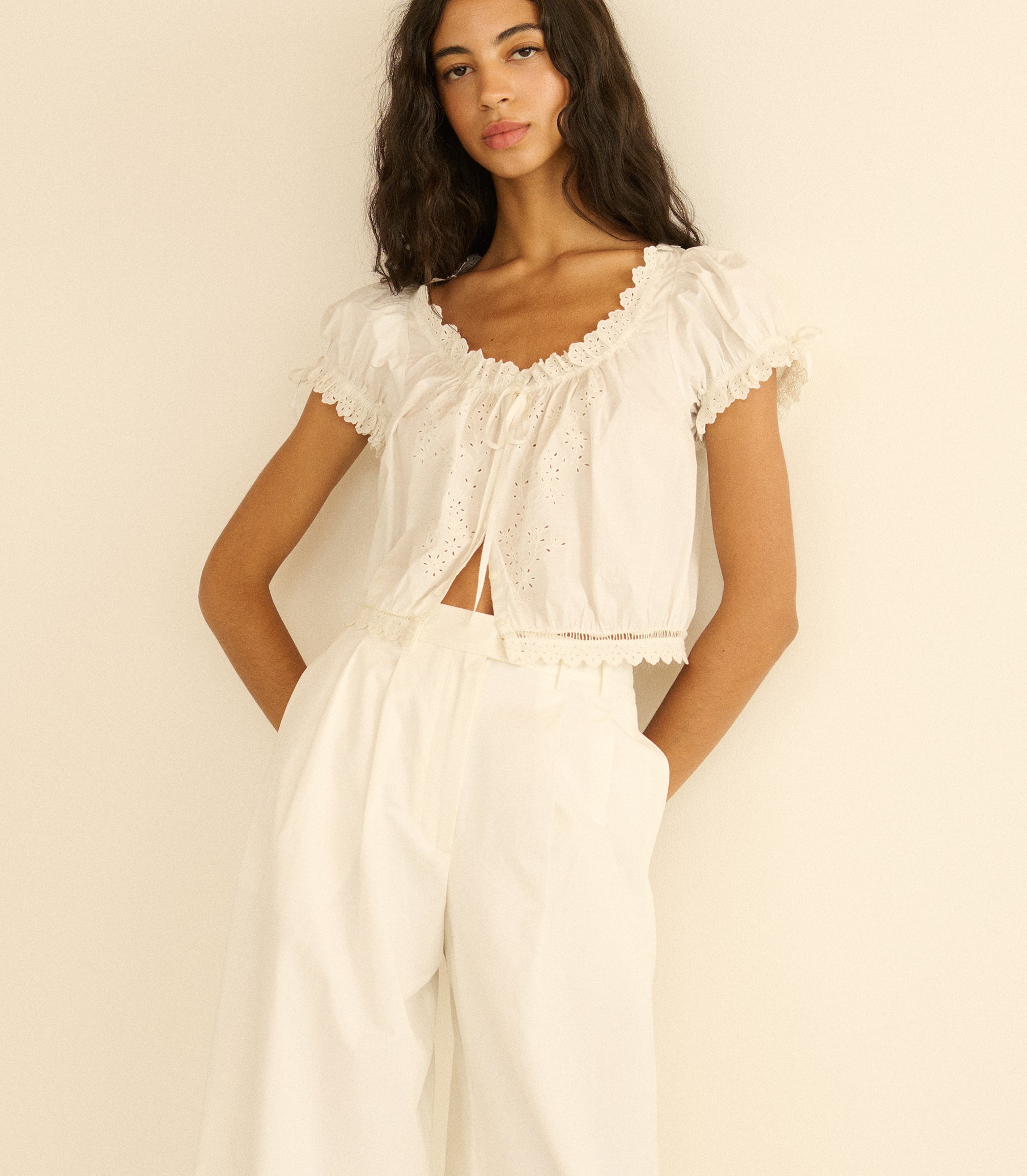 Woman wearing a white outfit with ruffled top and wide-leg pants against a beige background 1
