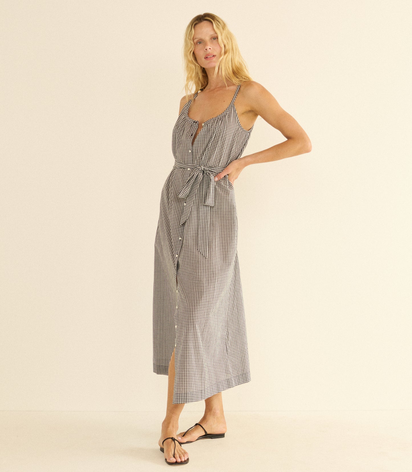 Woman wearing a black and white maxi dress and black sandals against a beige background