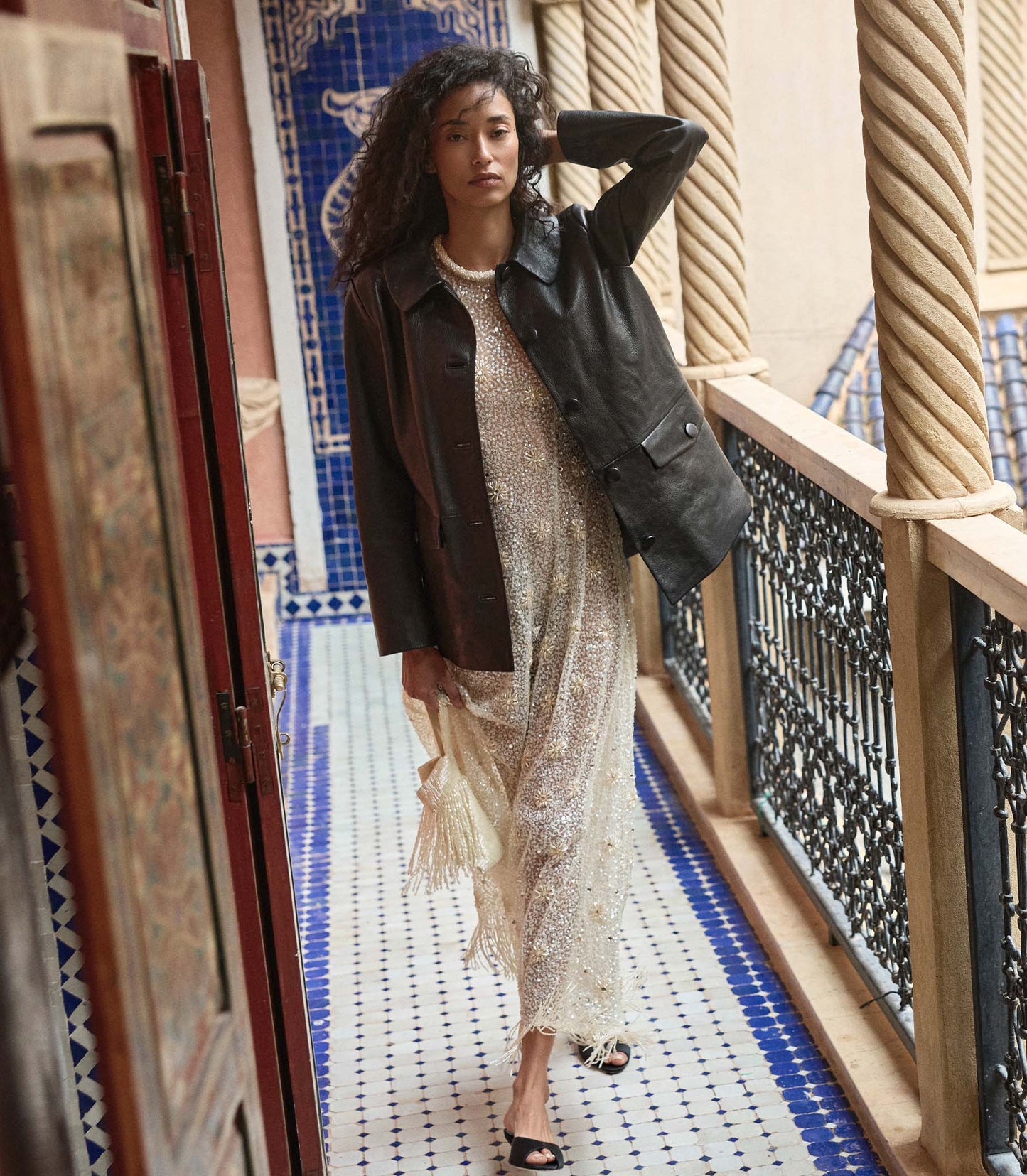 Woman in a stylish dress and black leather jacket standing on a balcony with decorative tiles.