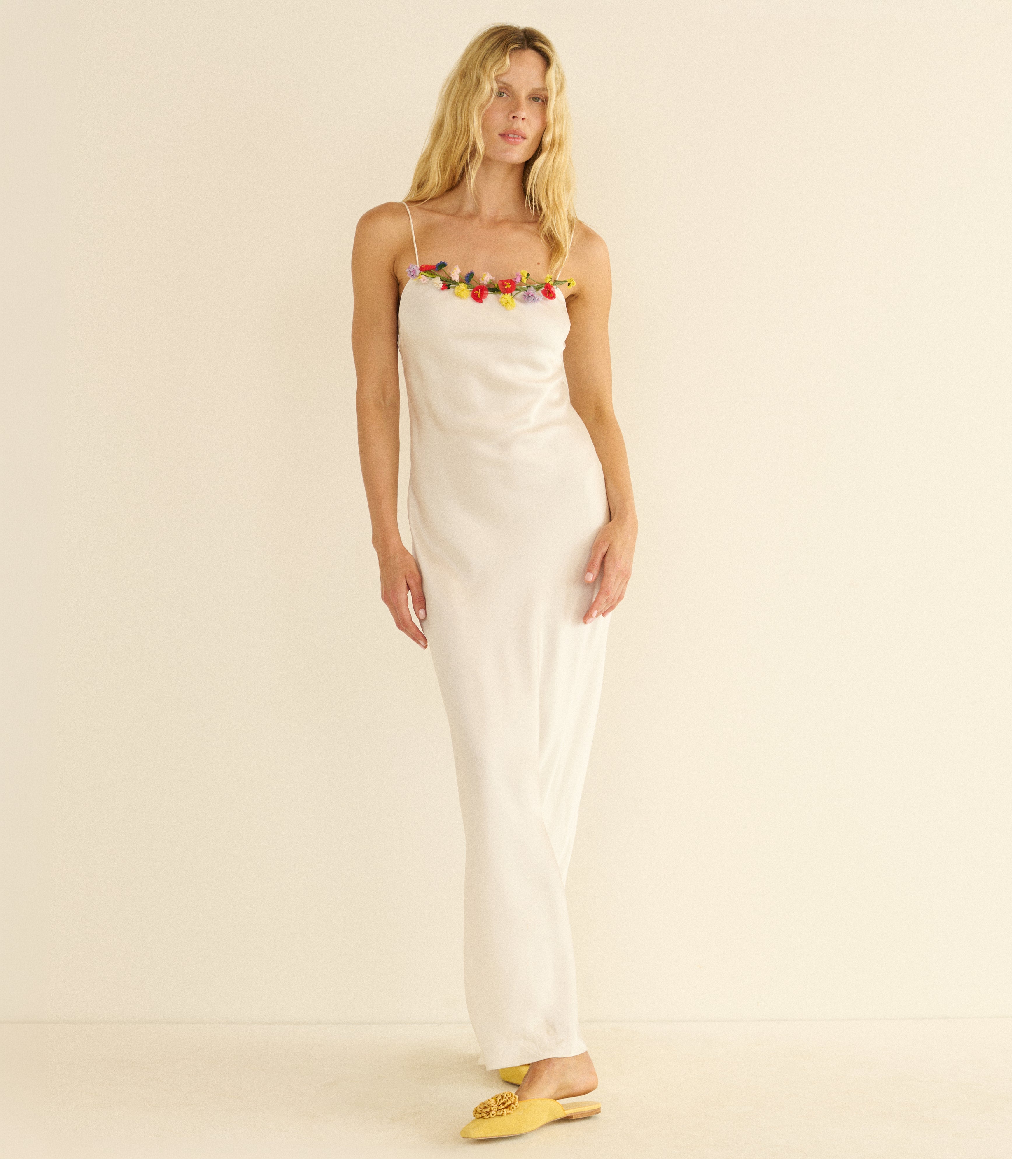 Woman wearing a white slip dress with colorful floral embellishments on a beige background
