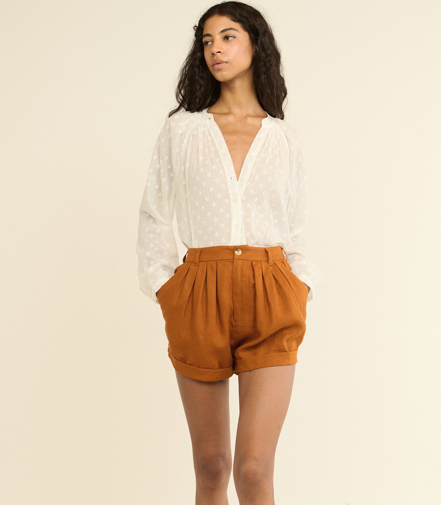 Woman wearing a white blouse and brown shorts on a beige background
