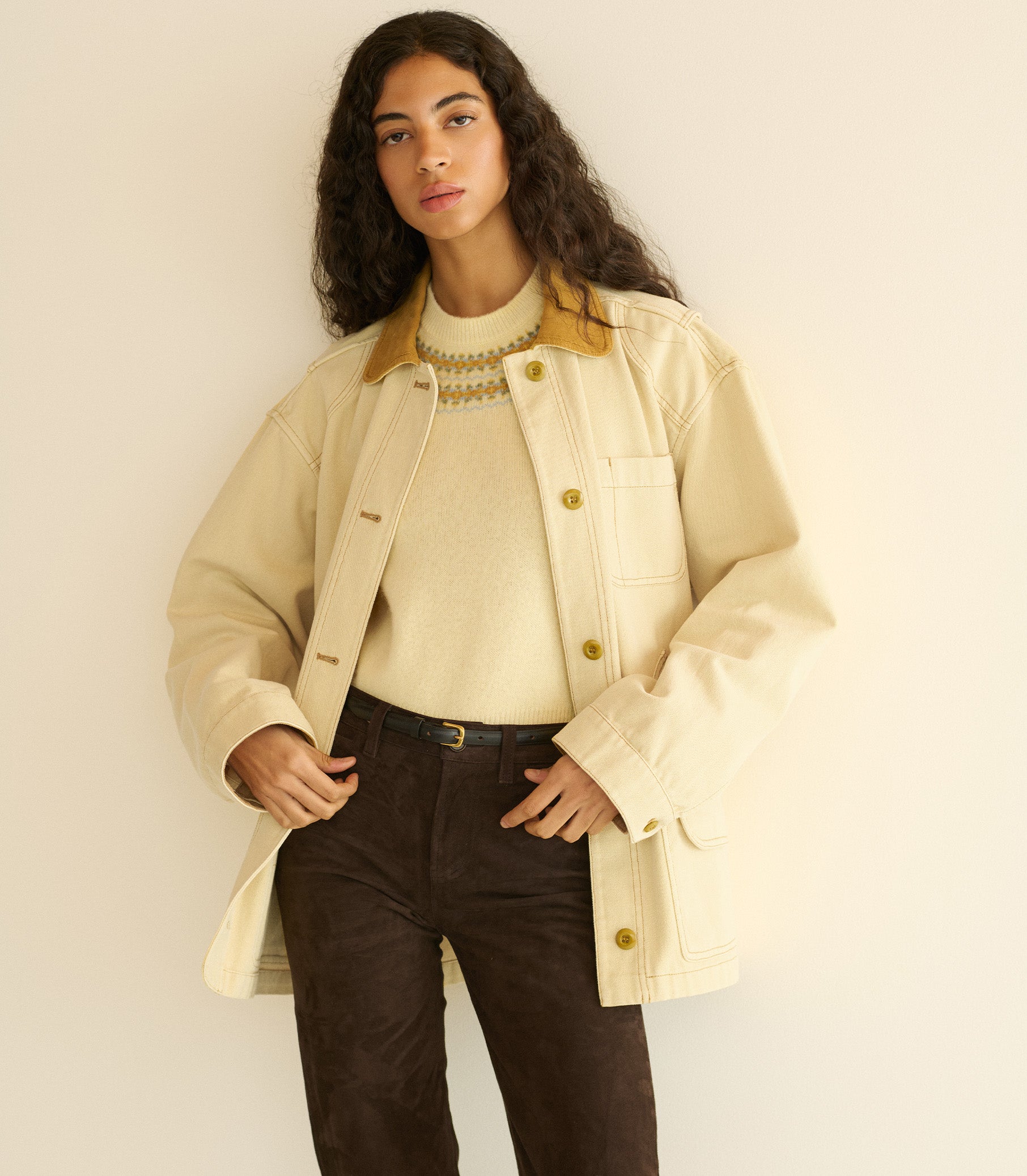 Woman wearing a light yellow barn jacket over a cream sweater and brown pants, standing against a plain background. 4
