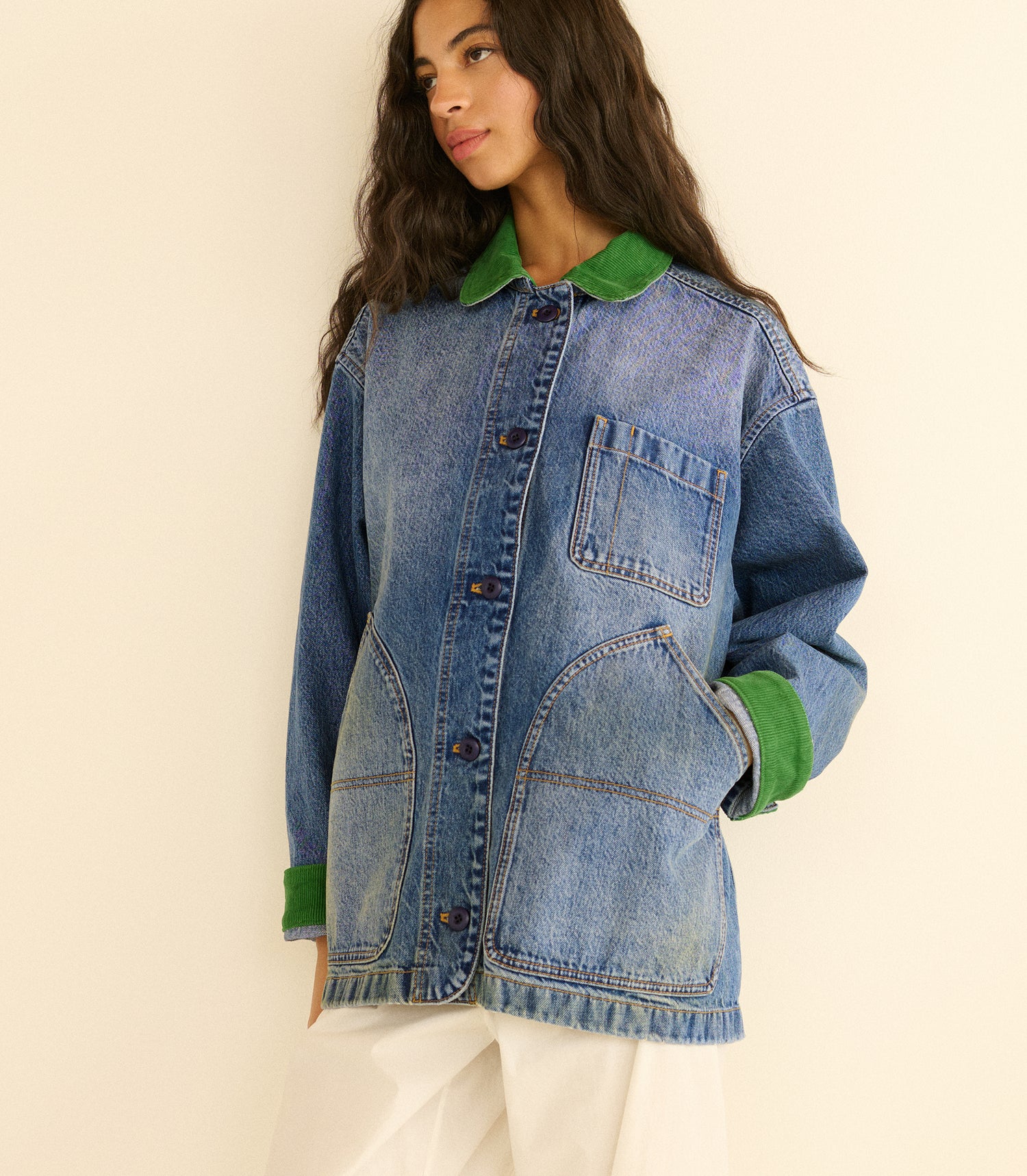 Person wearing a blue denim jacket with green collar and cuffs on a beige background