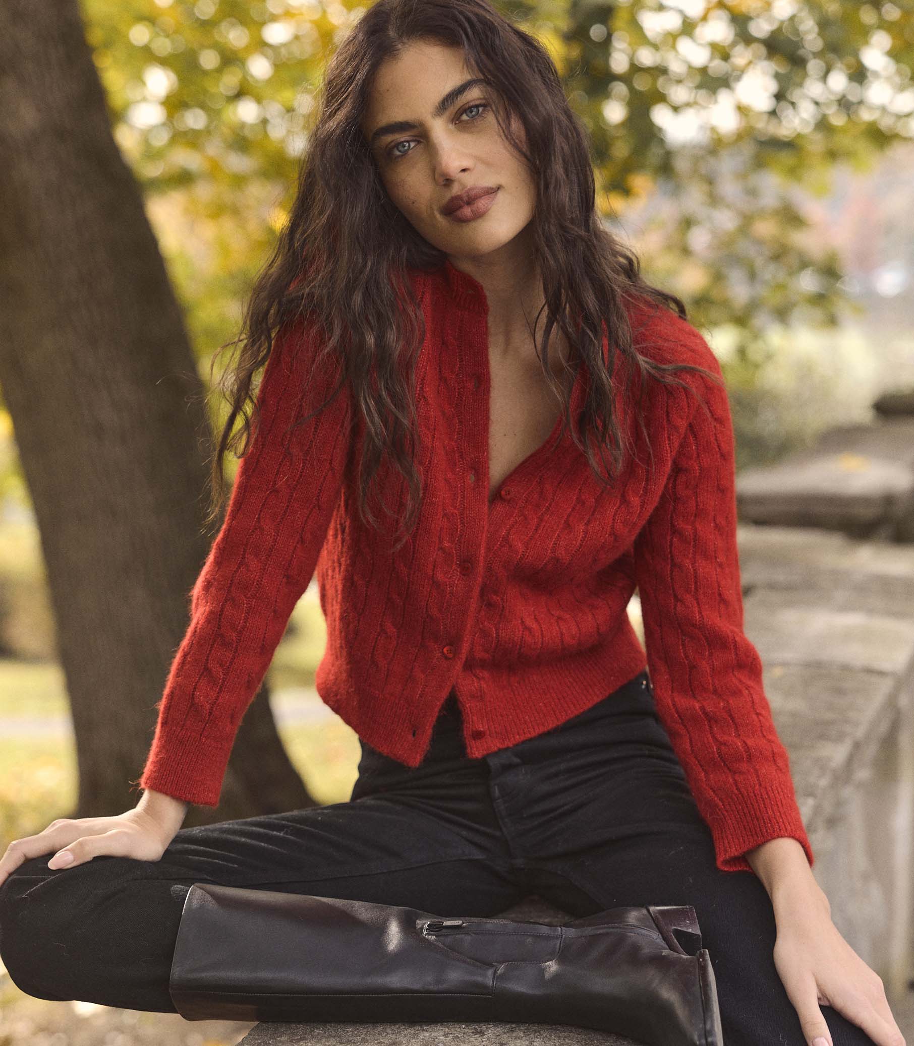 Woman wearing a red cardigan sitting outdoors with blurred greenery in the background 1
