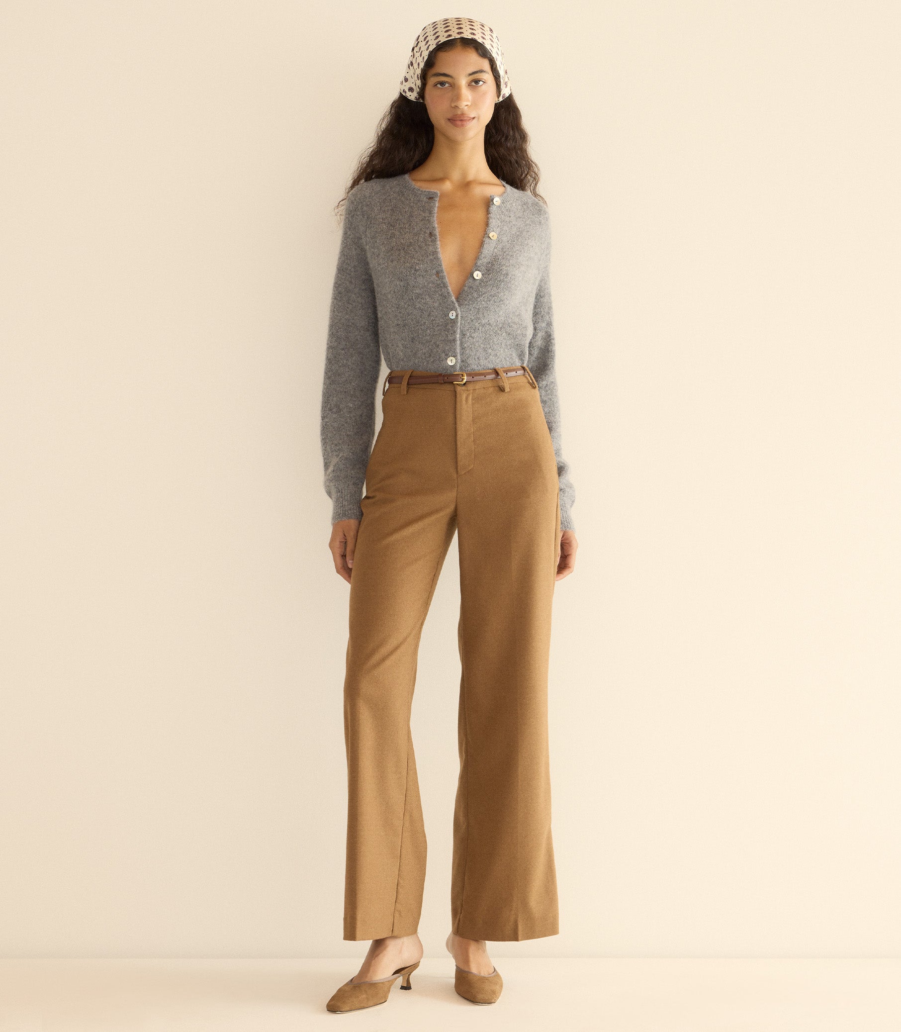 Woman wearing a gray cardigan and brown pants with a beige headband against a plain background 2
