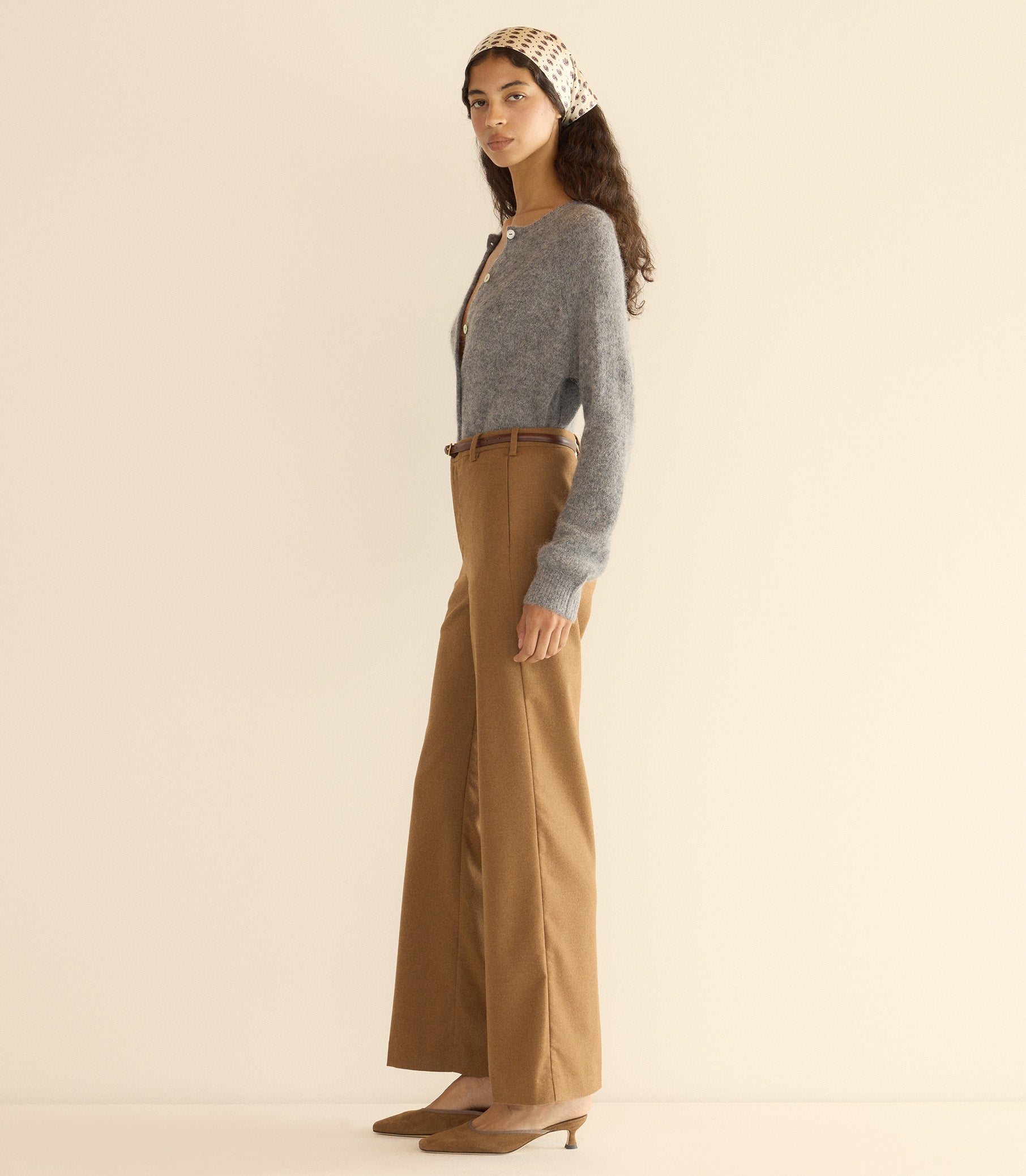 Woman wearing a gray cardigan and brown pants with a beige headband against a plain background 4
