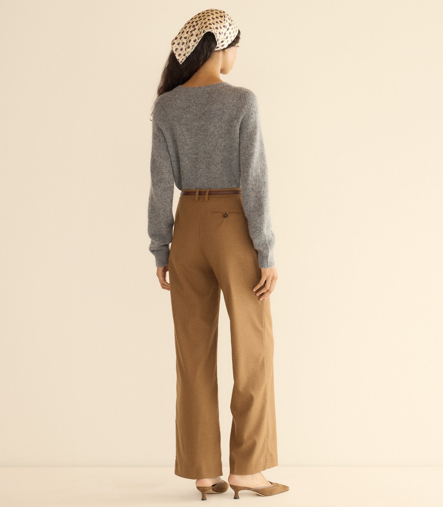 Woman wearing a gray cardigan and brown pants with a beige headband against a plain background