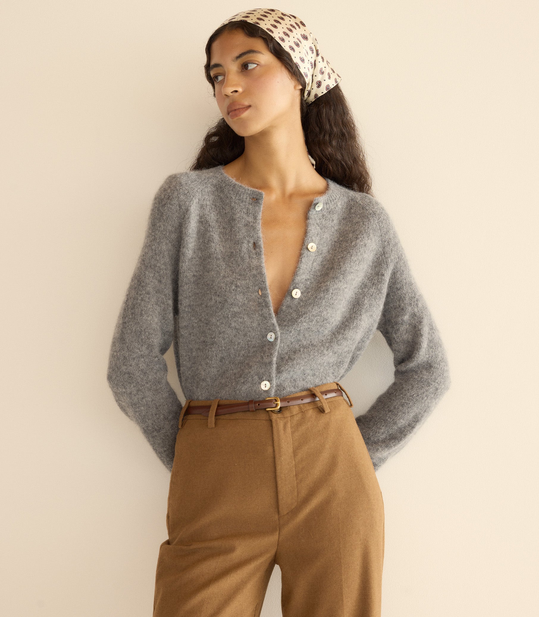 Woman wearing a gray cardigan and brown pants with a beige headband against a plain background 3

