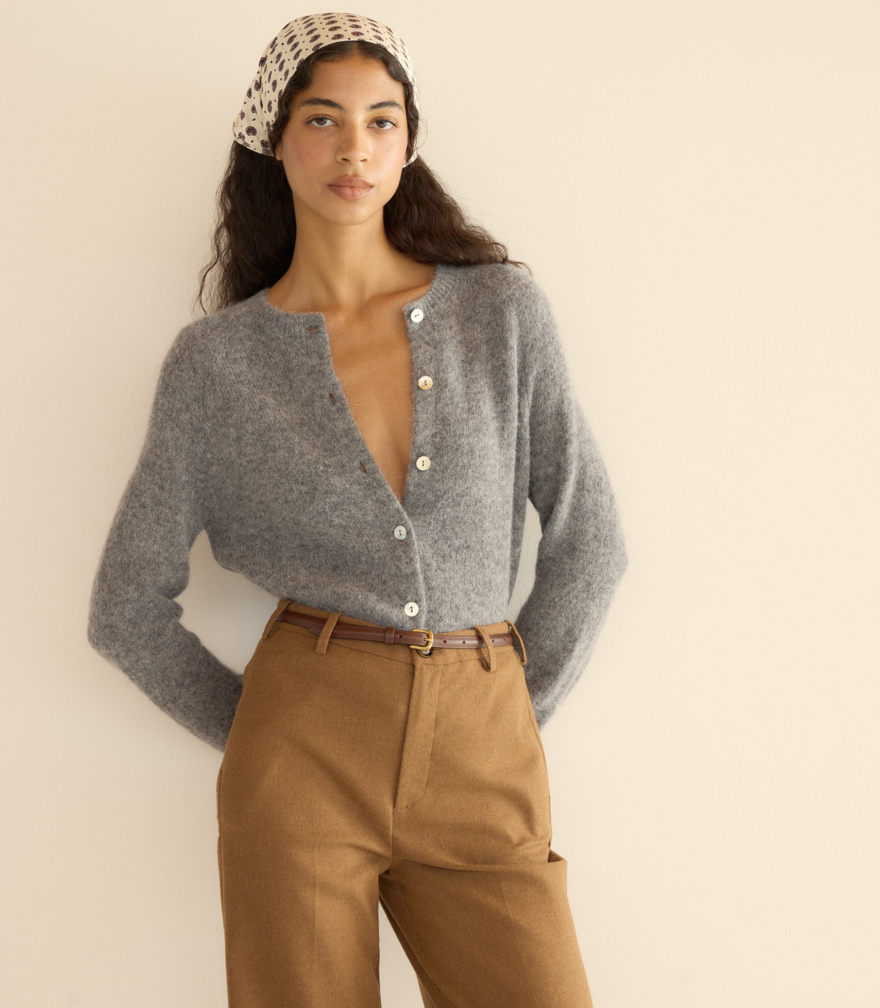 Woman wearing a gray cardigan and brown pants with a beige headband against a plain background 1
