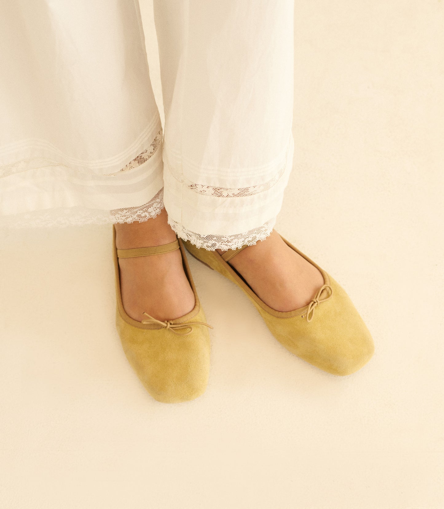 Yellow ballet flats worn with white pants on a light background