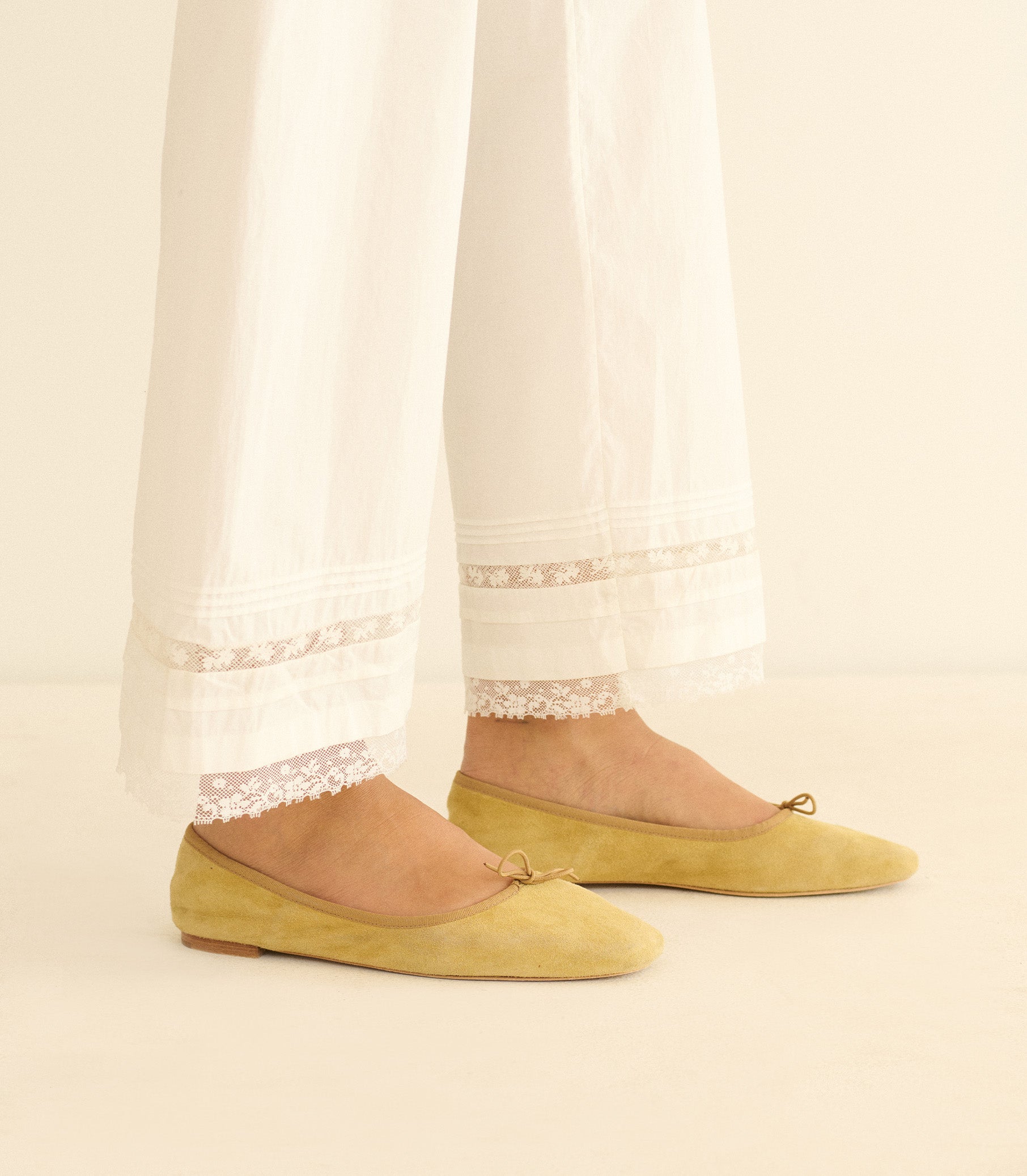 Yellow flats worn with white pants against a neutral background 2
