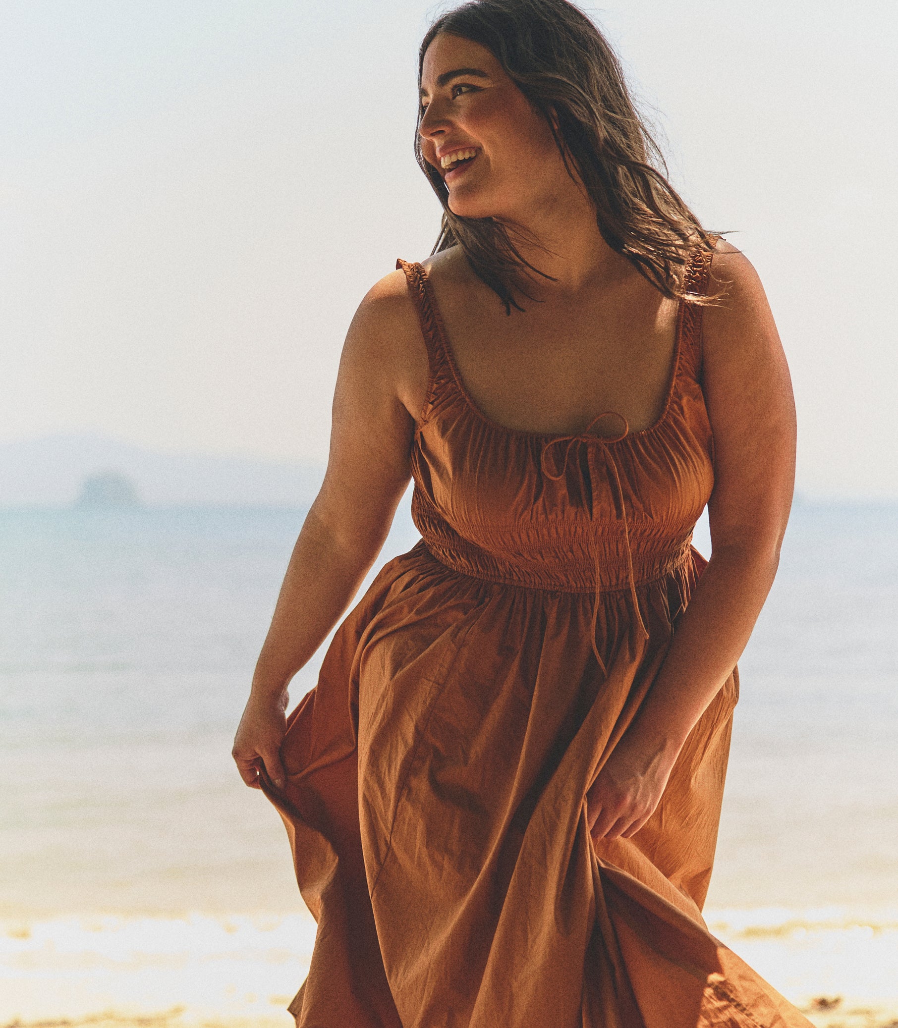 Woman in a rust-colored dress standing on a beach with a blurred background