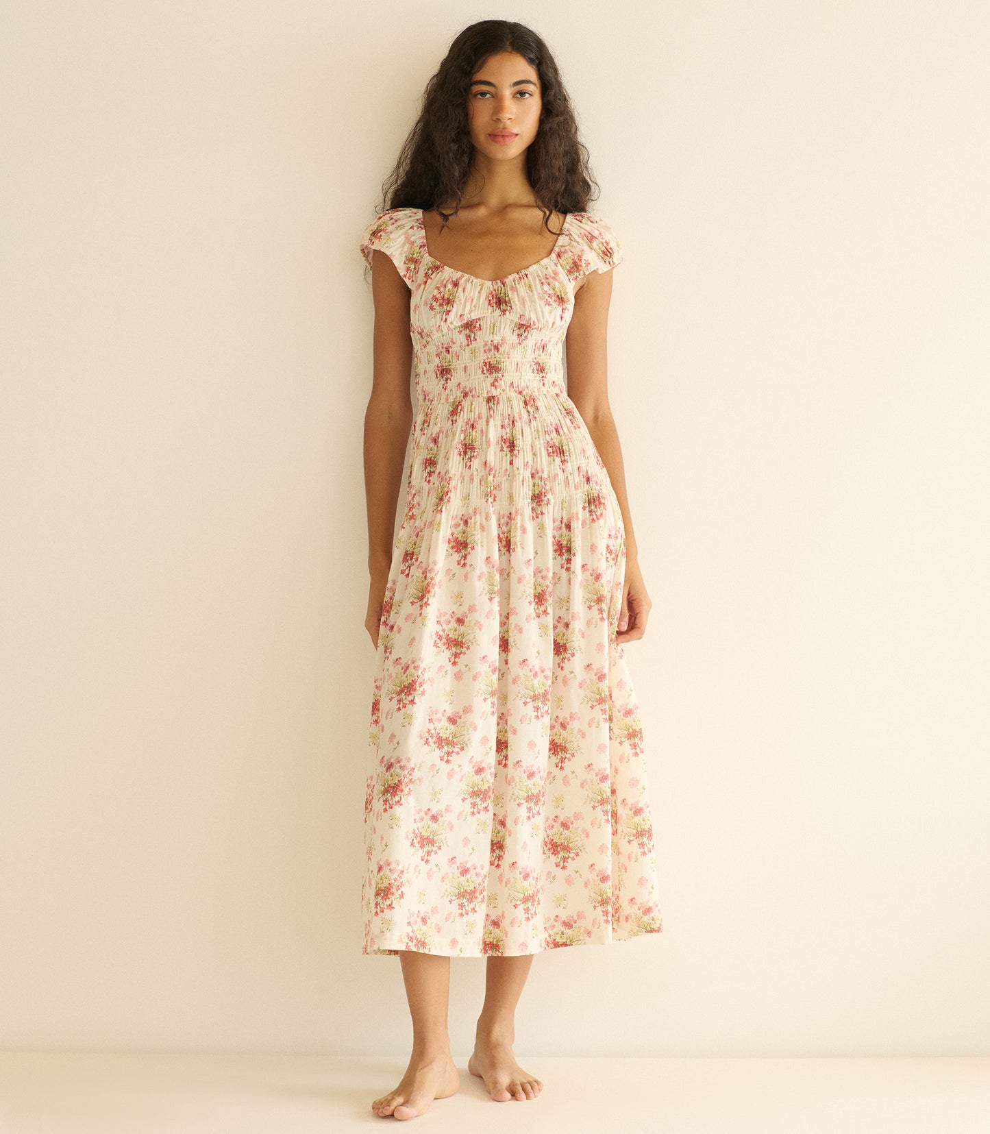 Woman wearing an ivory floral dress against a plain background
