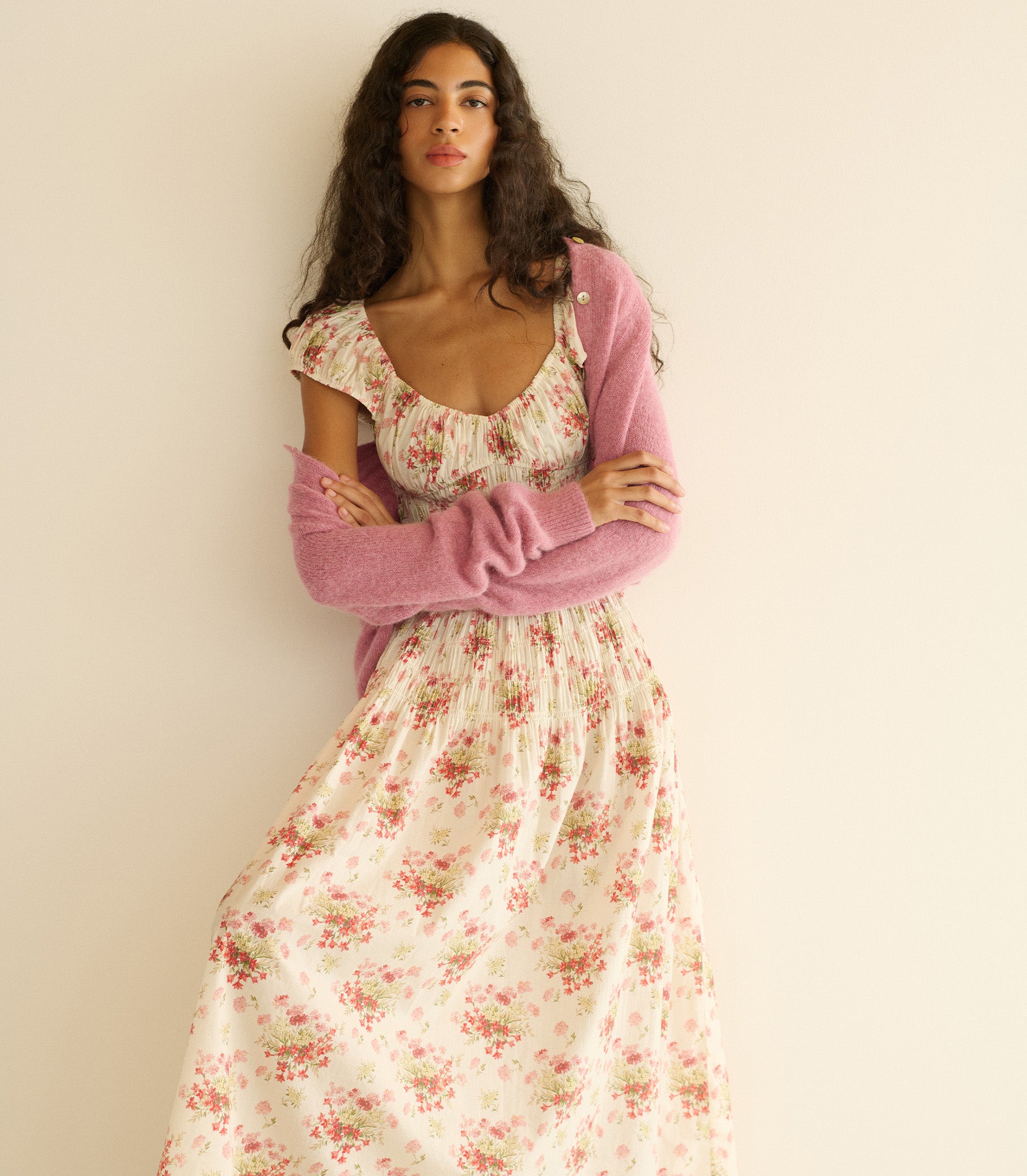 Woman wearing a white and pink floral dress with pink cardigan against a plain background 1
