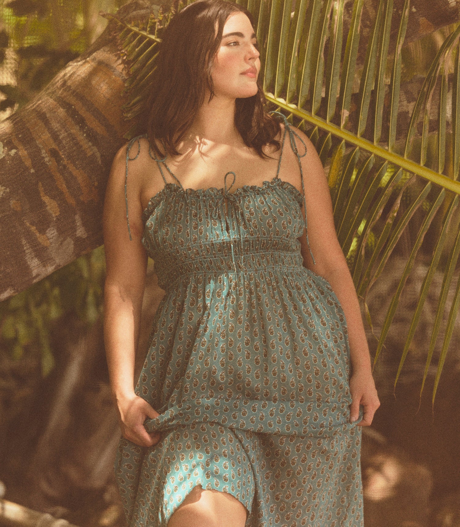 Woman in a green patterned dress standing among palm leaves
