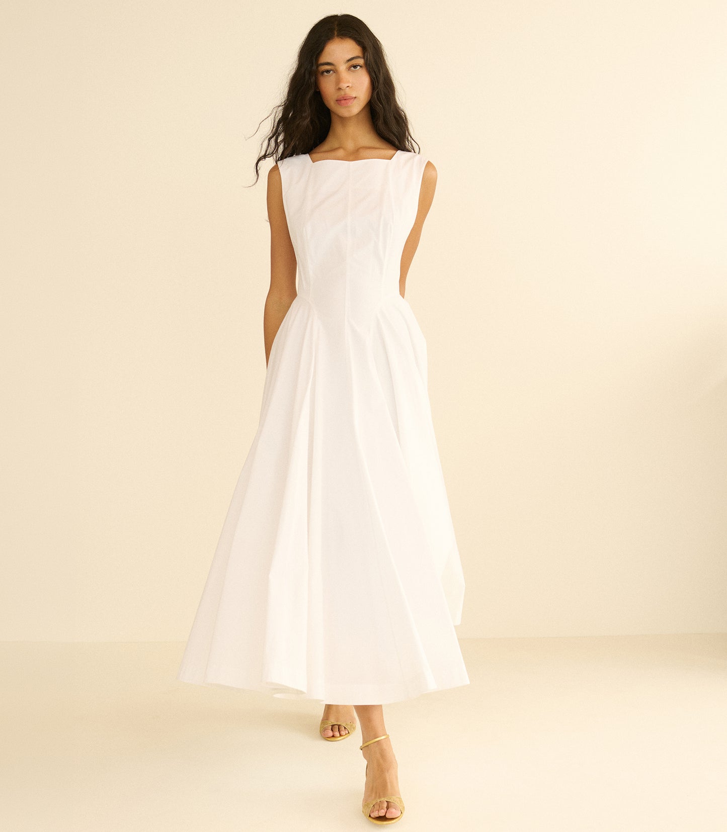 Woman wearing a long white dress against a beige background