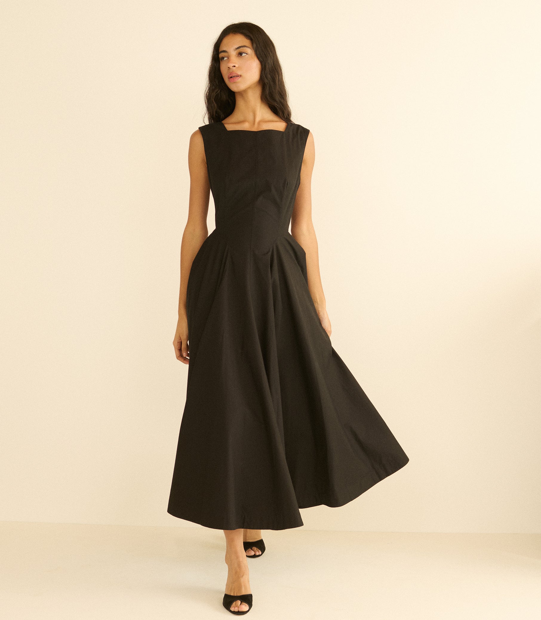 Woman wearing a long black dress against a beige background 1
