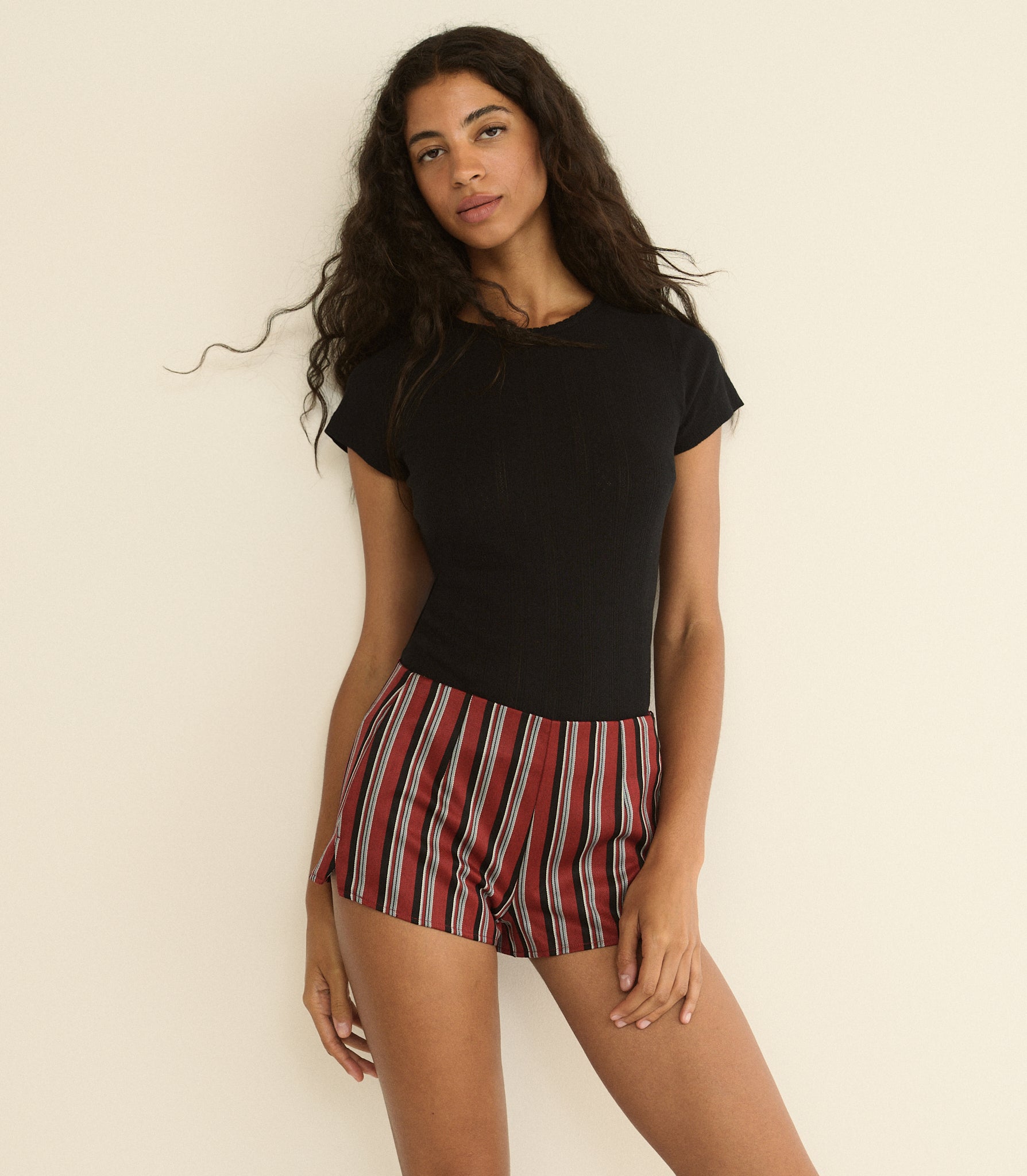 Woman wearing a black top and red striped shorts against a beige background 1

