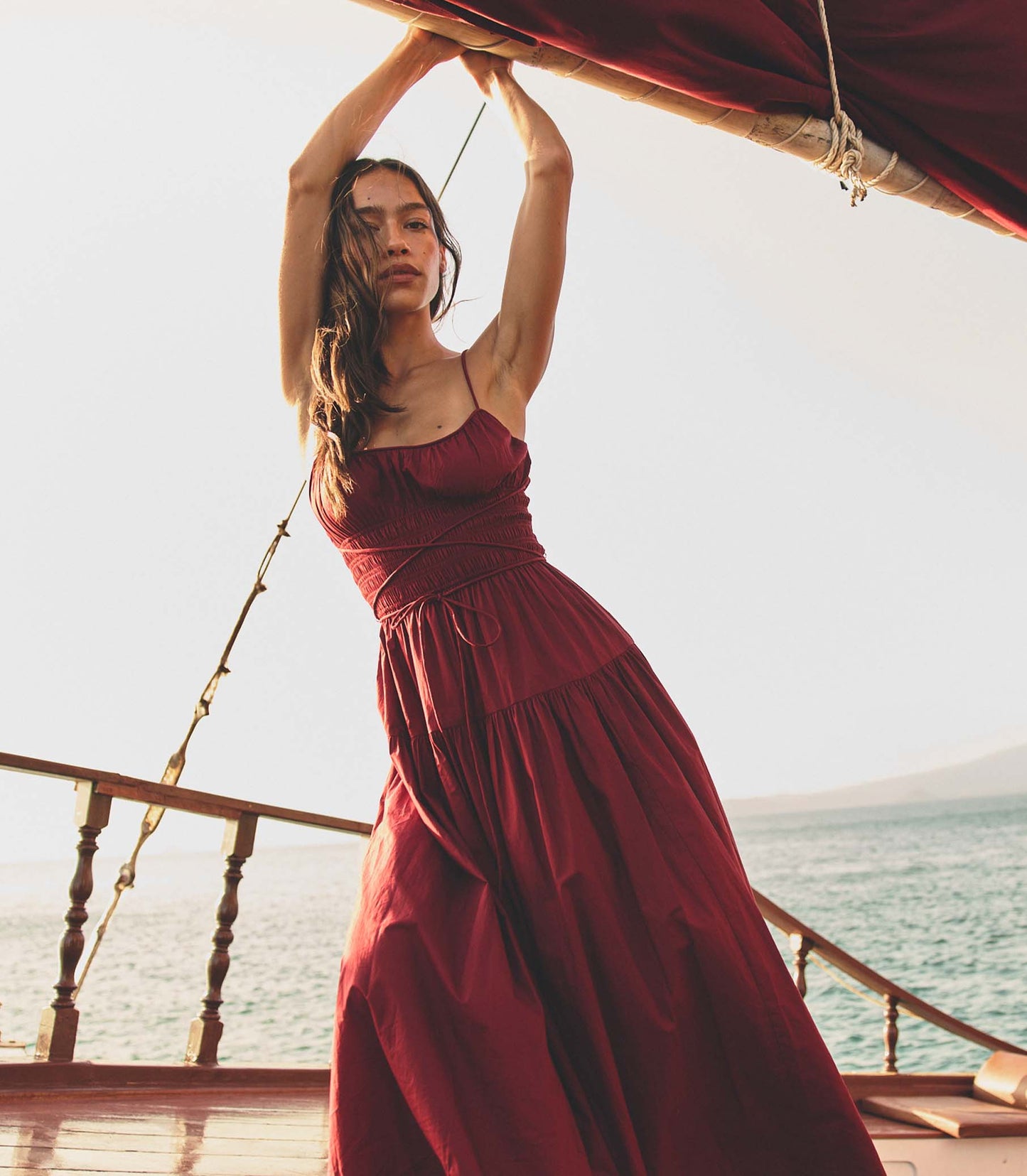Woman in a deep red dress standing on a boat with ocean view