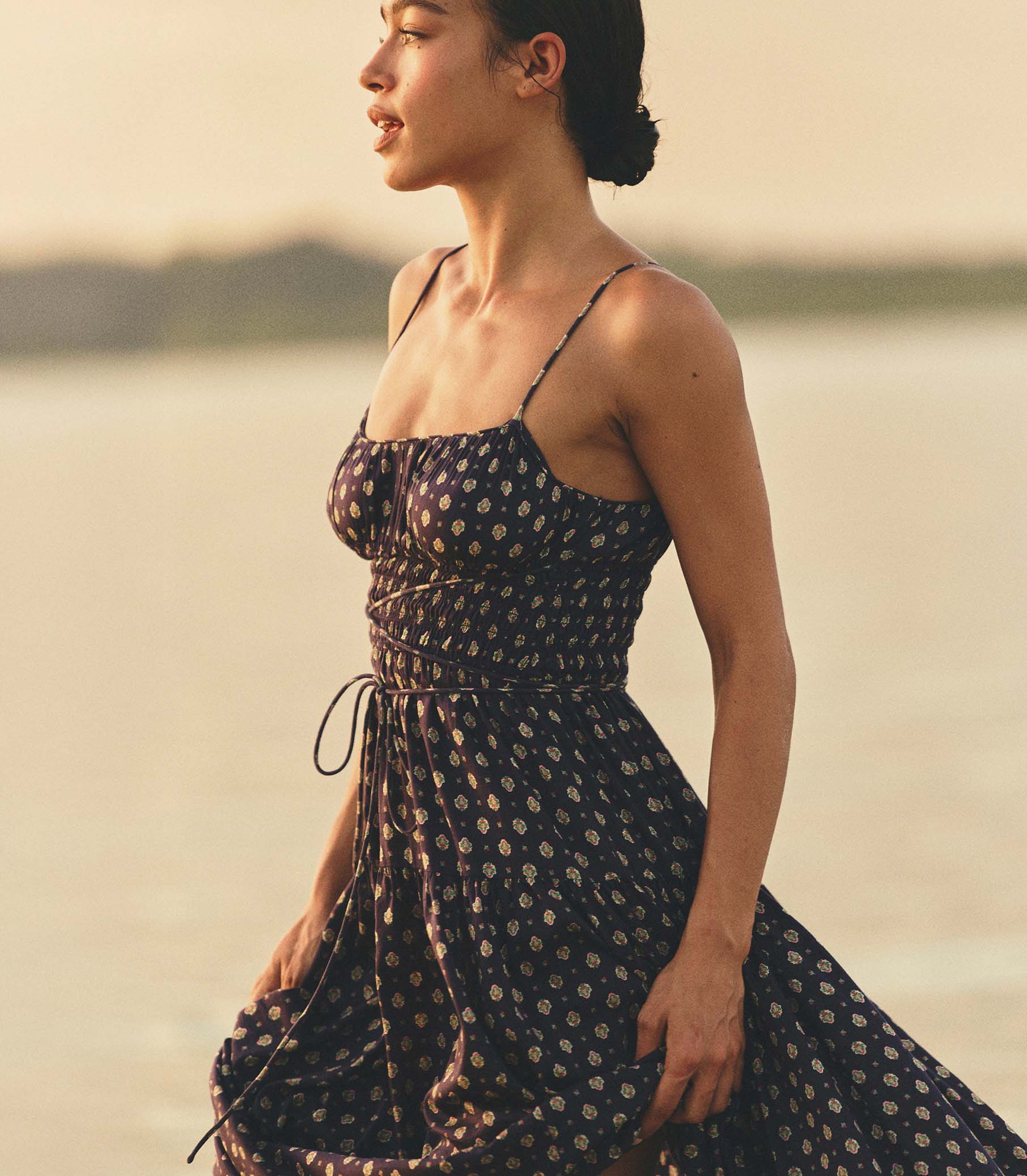 Woman in a navy foulard dress standing on a beach at sunset. 1
