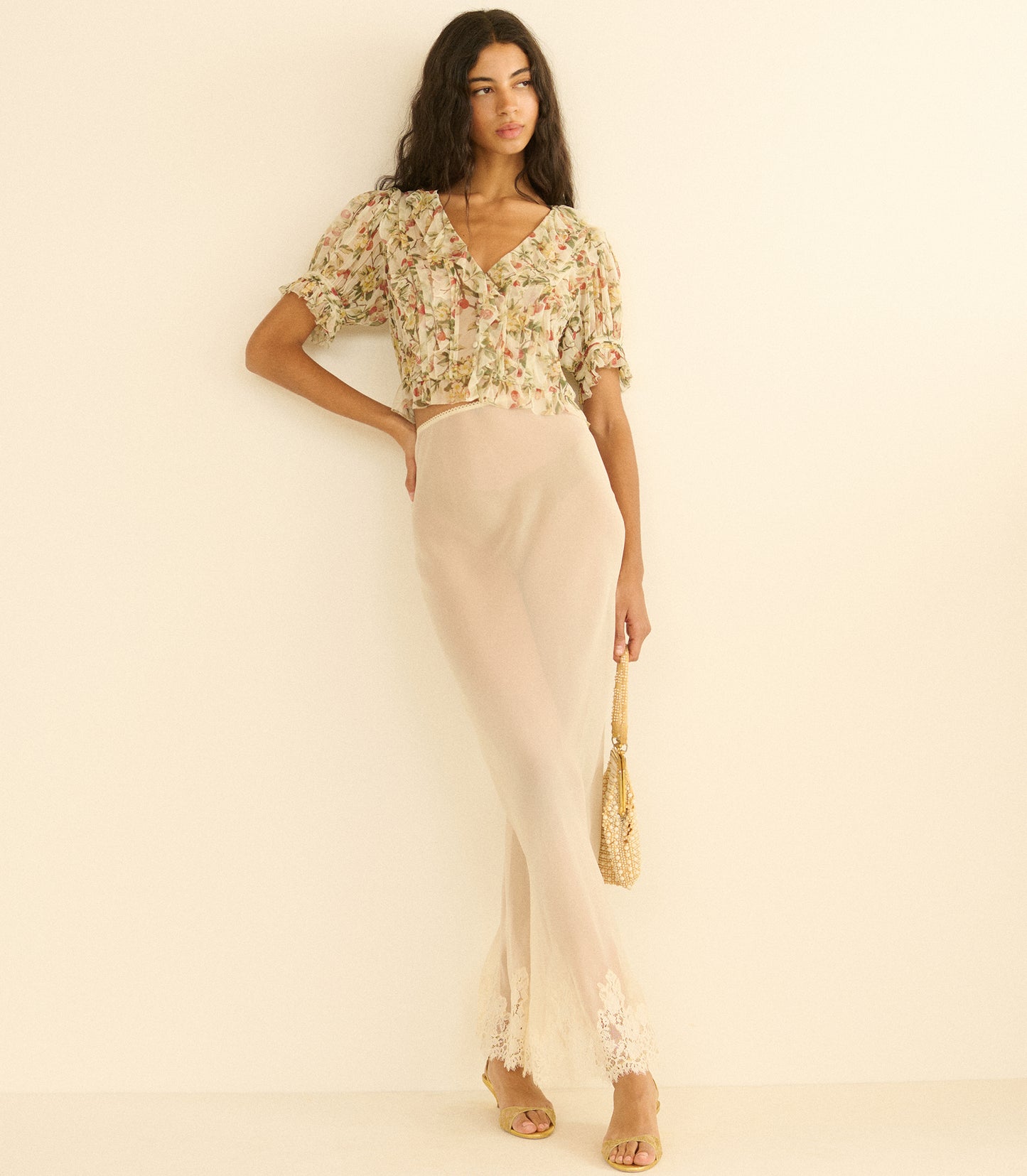 Woman wearing a floral top and beige pants against a plain background