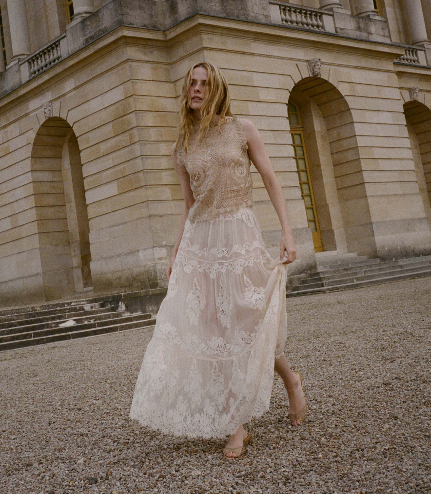 Woman in a white lace skirt standing in front of a classical building. 1
