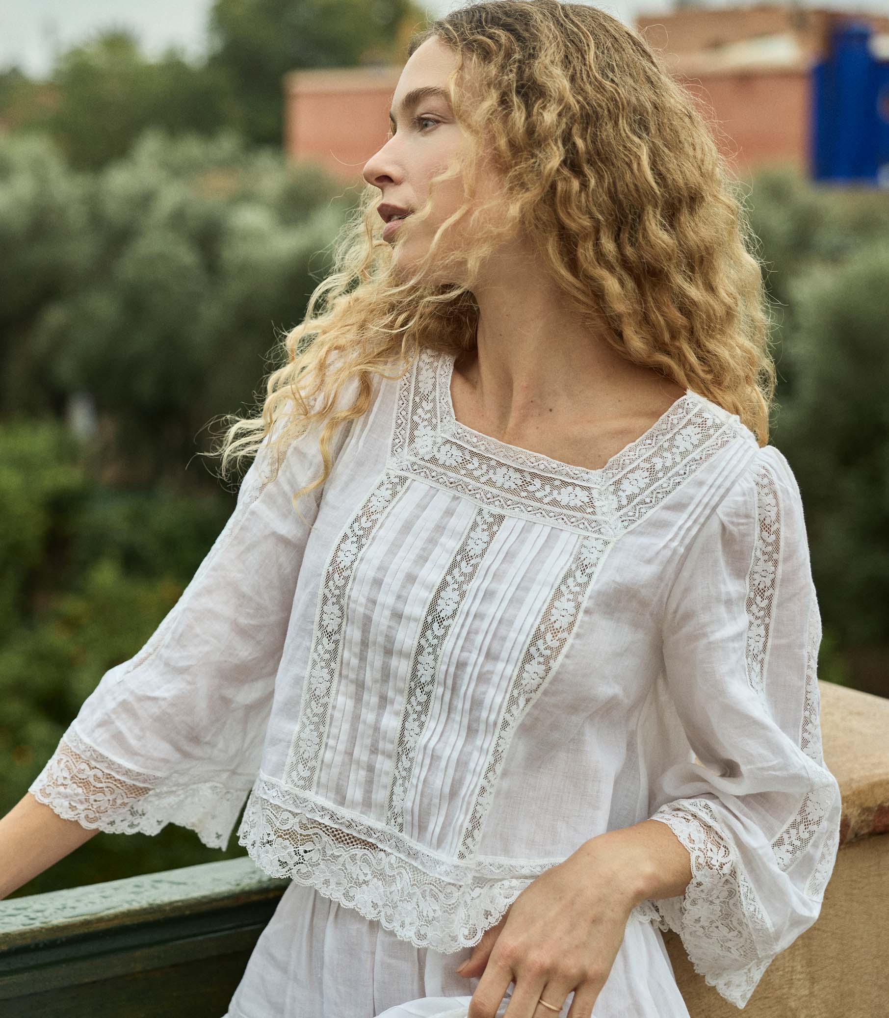 Woman wearing a white embroidered blouse outdoors with greenery in the background