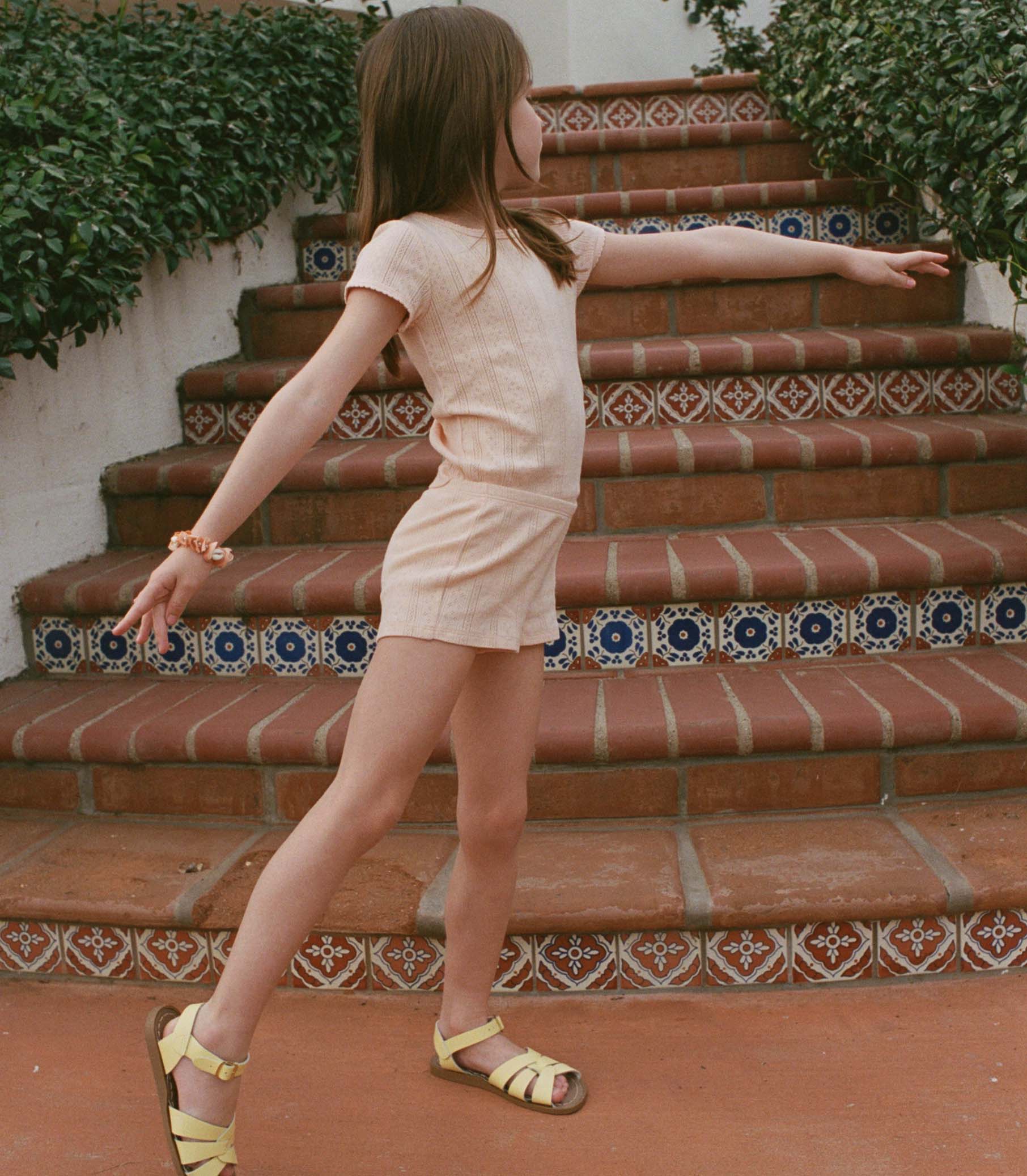 Young girl in a peach outfit standing on a set of decorative brick steps. 1
